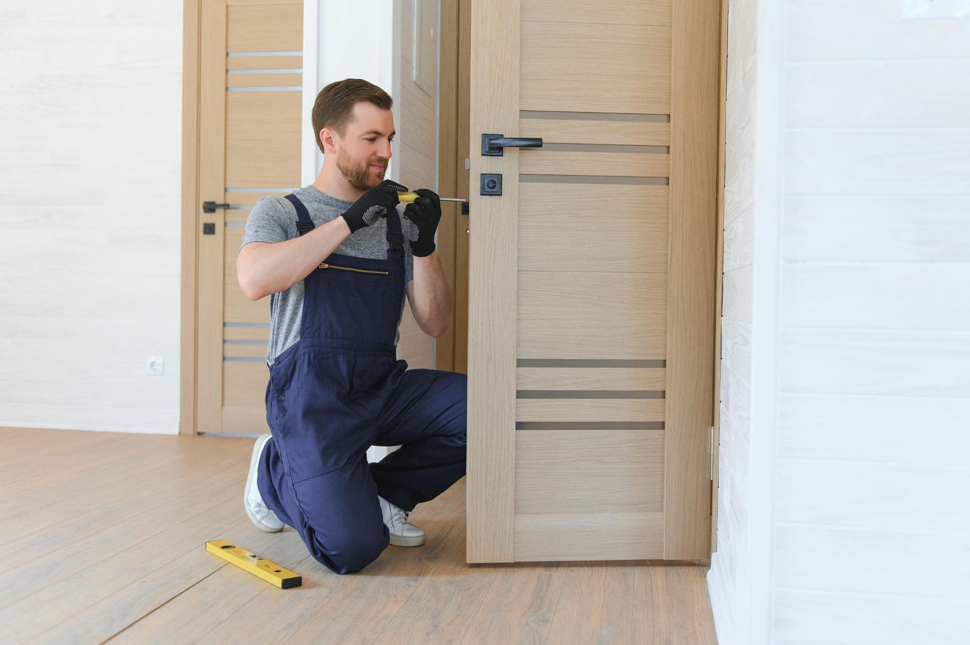 Man in blue jumpsuit installing a door handle with a screwdriver. 