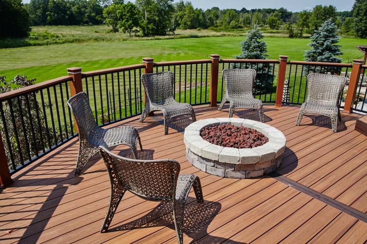 Deck with a stone fire pit and woven chairs, overlooking a grassy field.