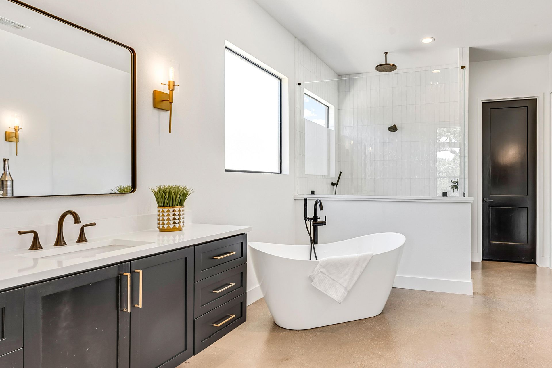 Modern bathroom with black vanity, white tub, shower, and black door.