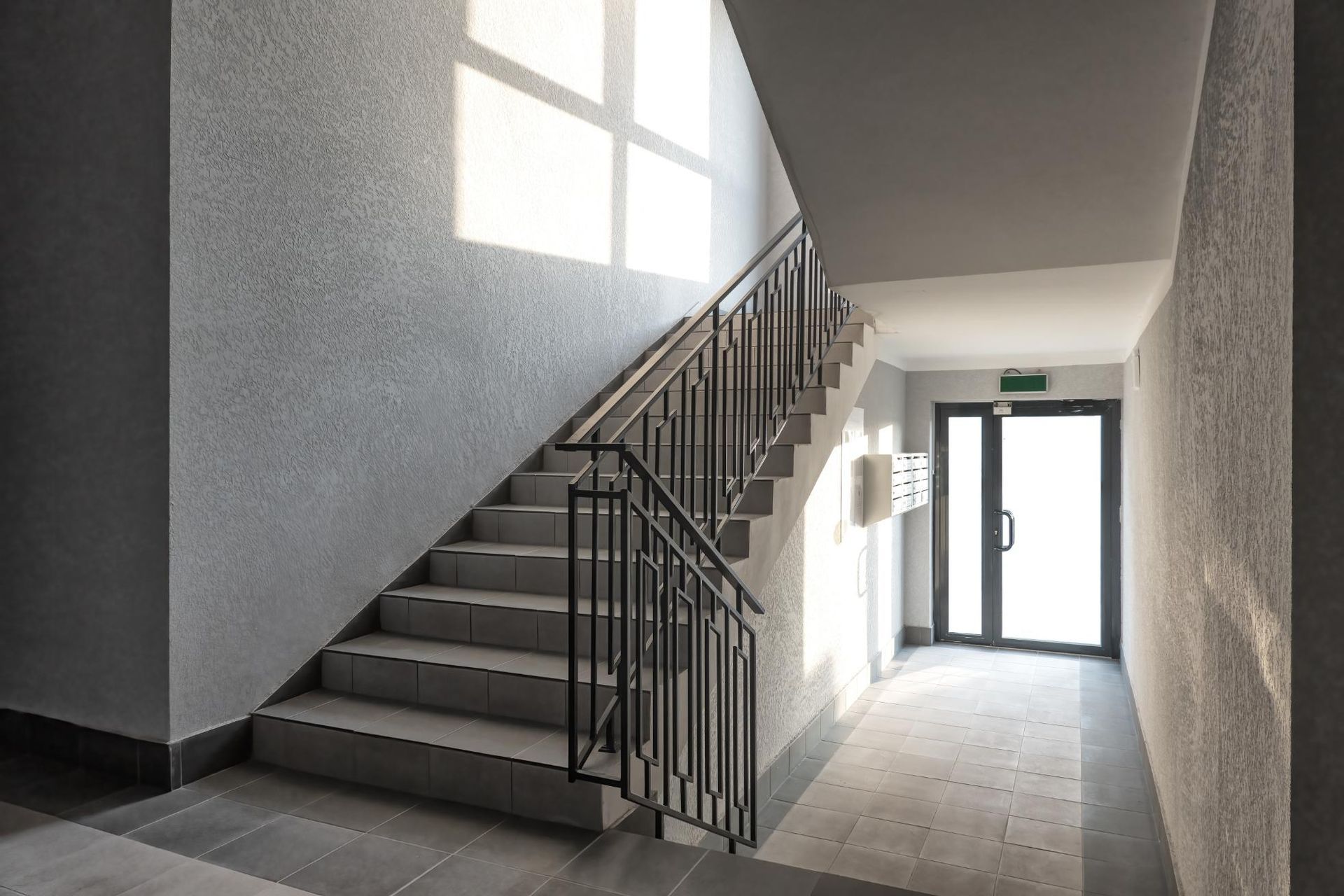 Staircase in a building hallway, with sunlight from a window illuminating the stairs and doorway.