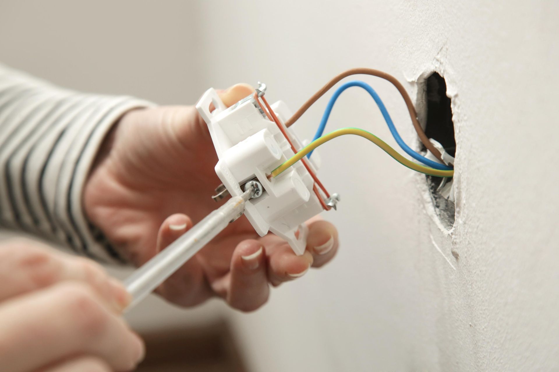 Person installing an electrical outlet, with colored wires and a screwdriver.