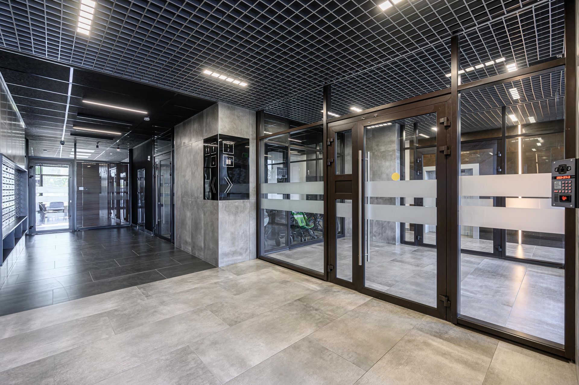 Modern lobby with glass doors, gray tile floors, and a metal grid ceiling.