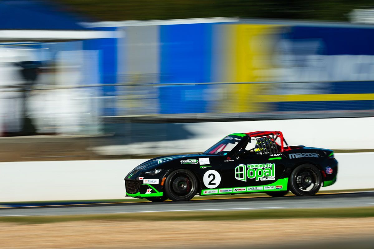 Max Opalski's black and green Mazda MX-5 race car driving down a race track.
