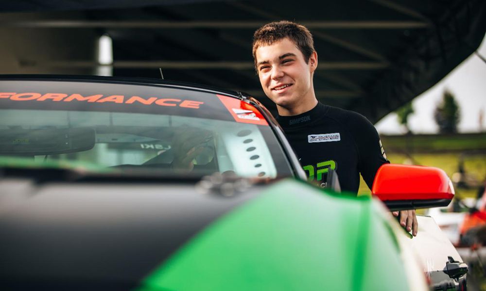 Max Opalski is standing next to his green and black Mustang.