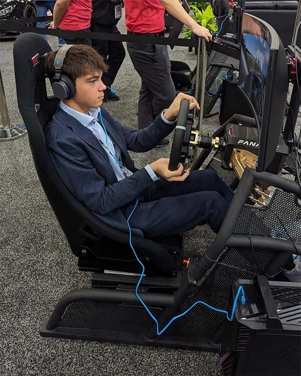Max Opalski in a suit is sitting in a SIM racing setup and focussed on the race.