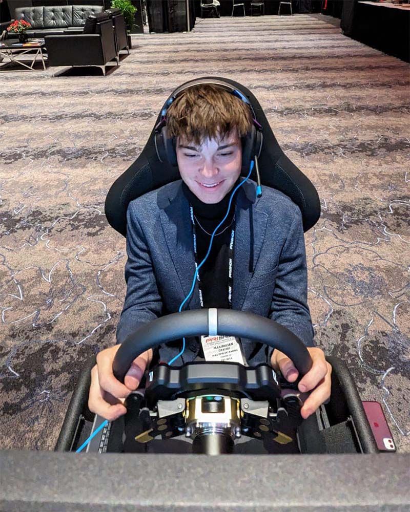Max Opalski wearing headphones is sitting in a SIM racing rig and similes during his winning lap.