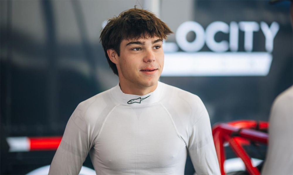 Max Opalski in a white shirt is sitting in a garage smiling.