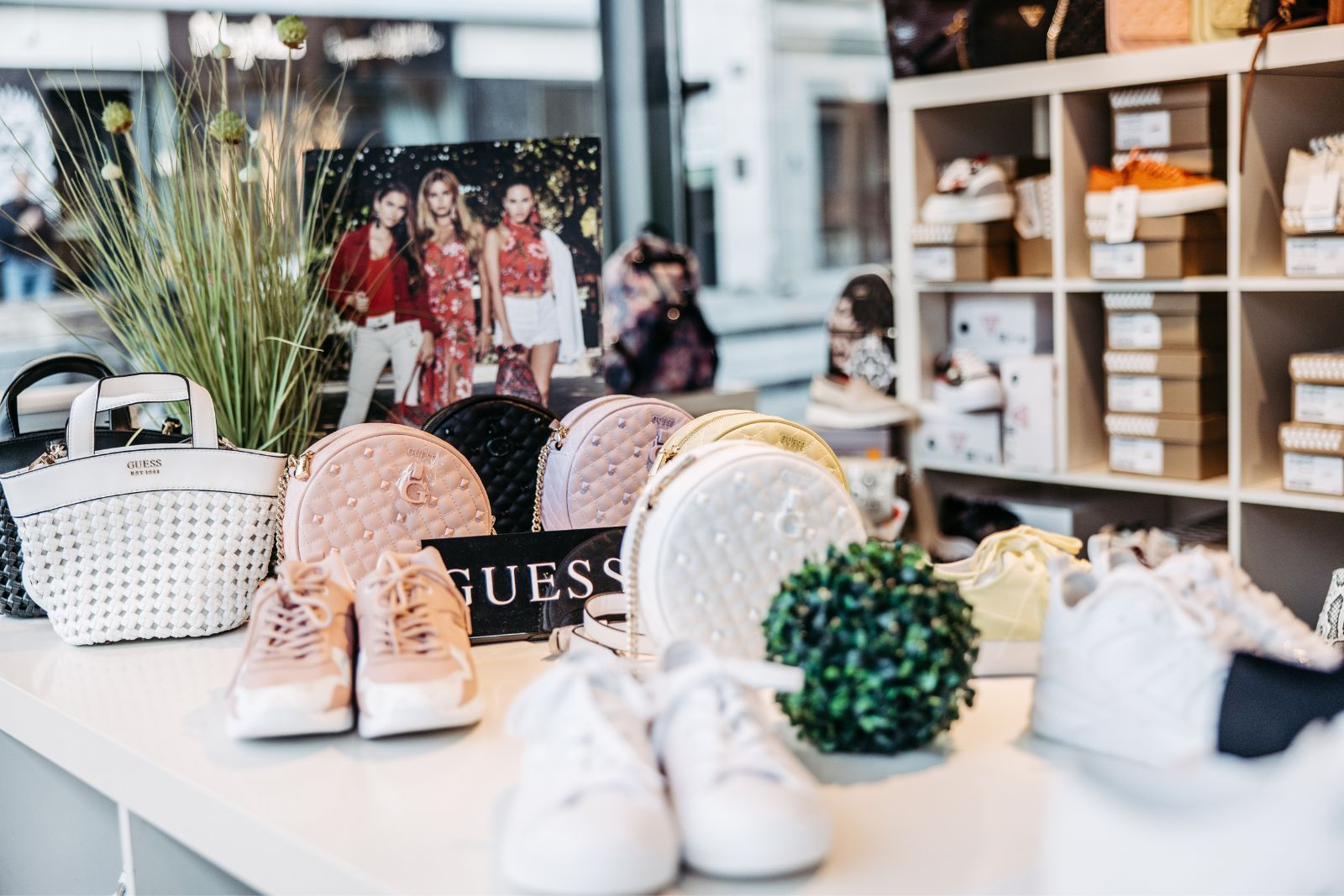 Eine Auslage mit Schuhen und Taschen von Guess auf einem Tisch in einem Geschäft.