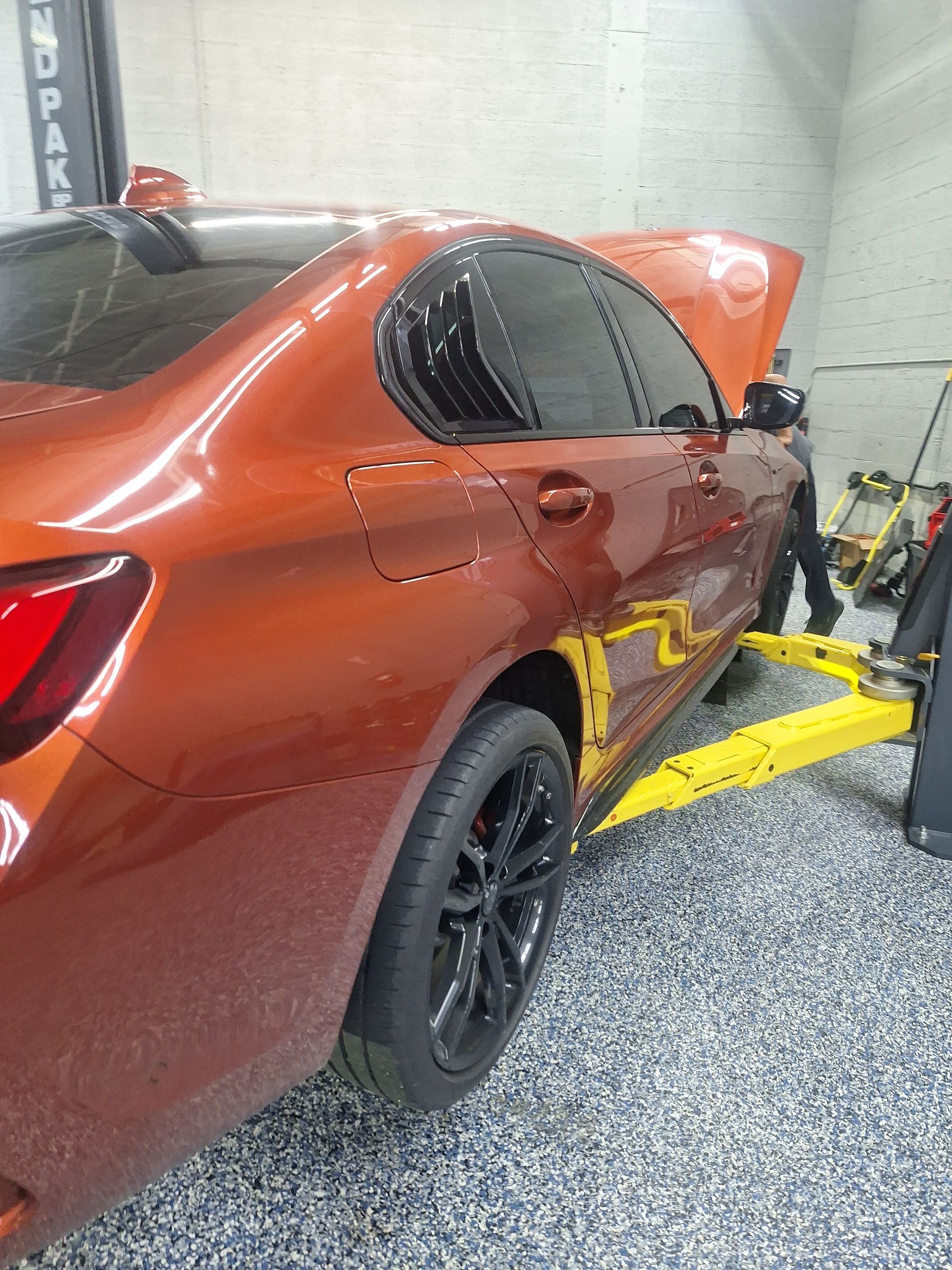Orange sedan on a lift in a garage, with its hood open and a wheel removed | Temis Motorsports