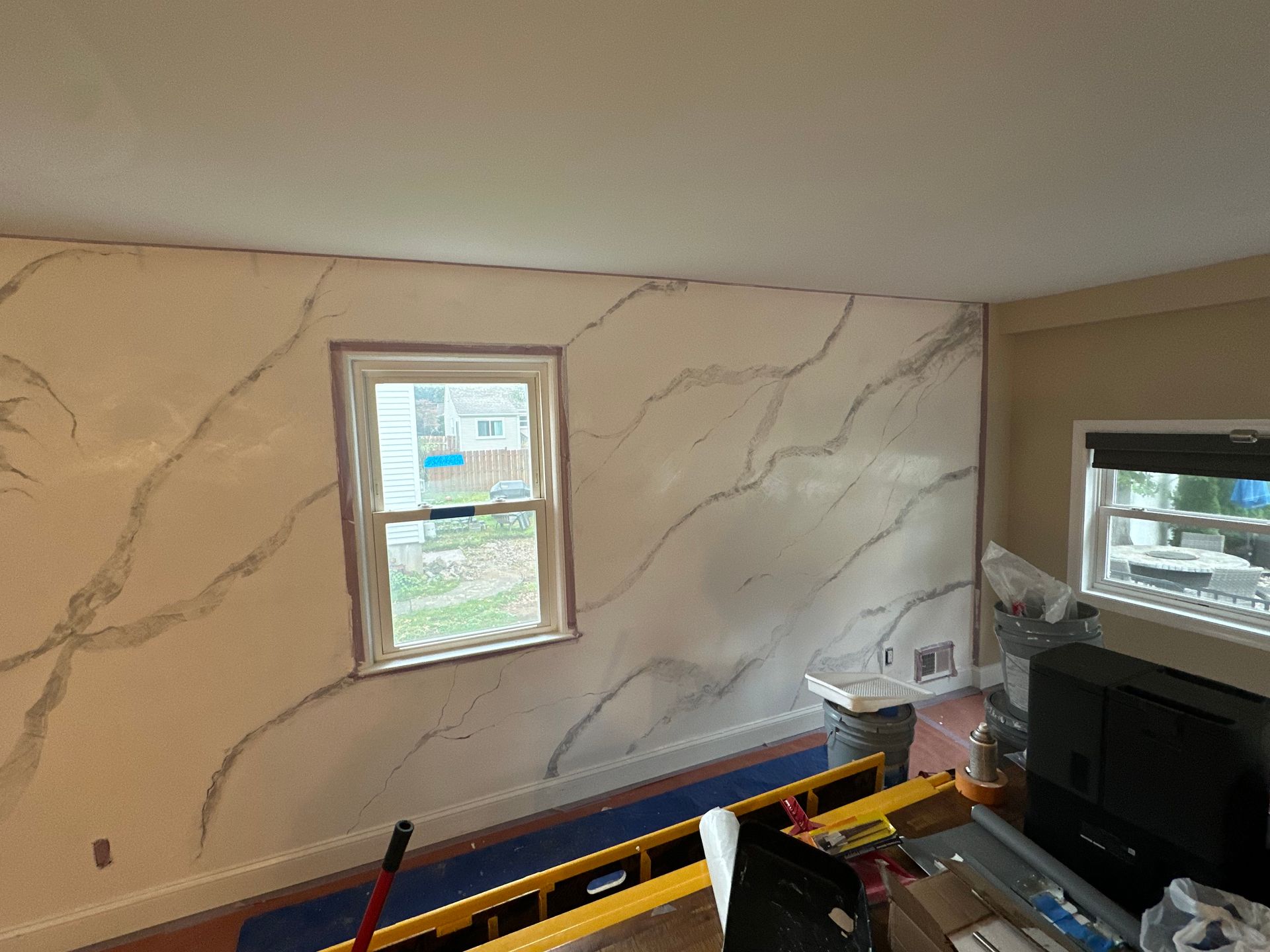 Small room with marble-pattern wallpaper, two windows, and construction tools near a TV.