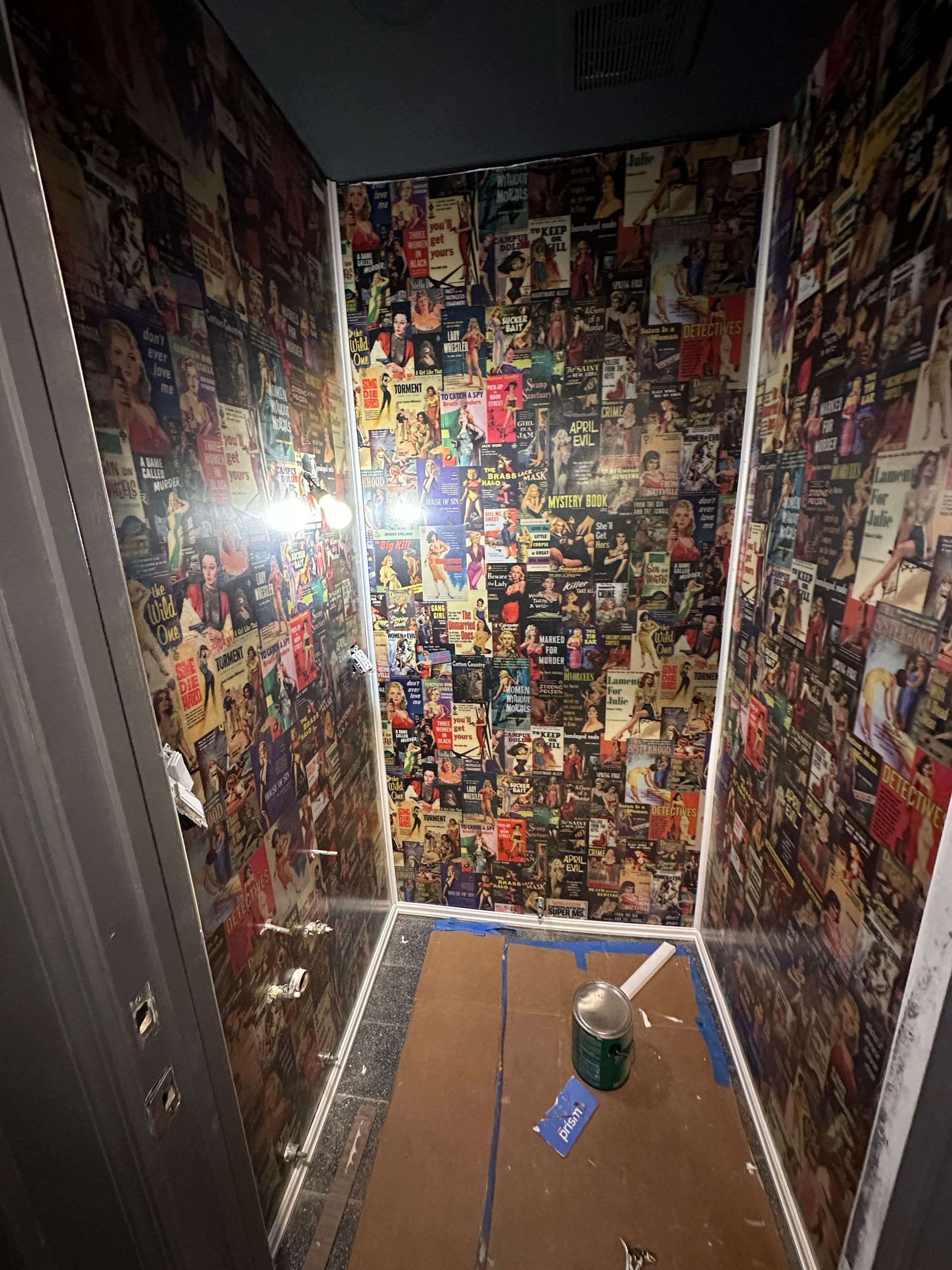 Small hallway covered in colorful collage posters, with a bucket and blue tape on the floor.