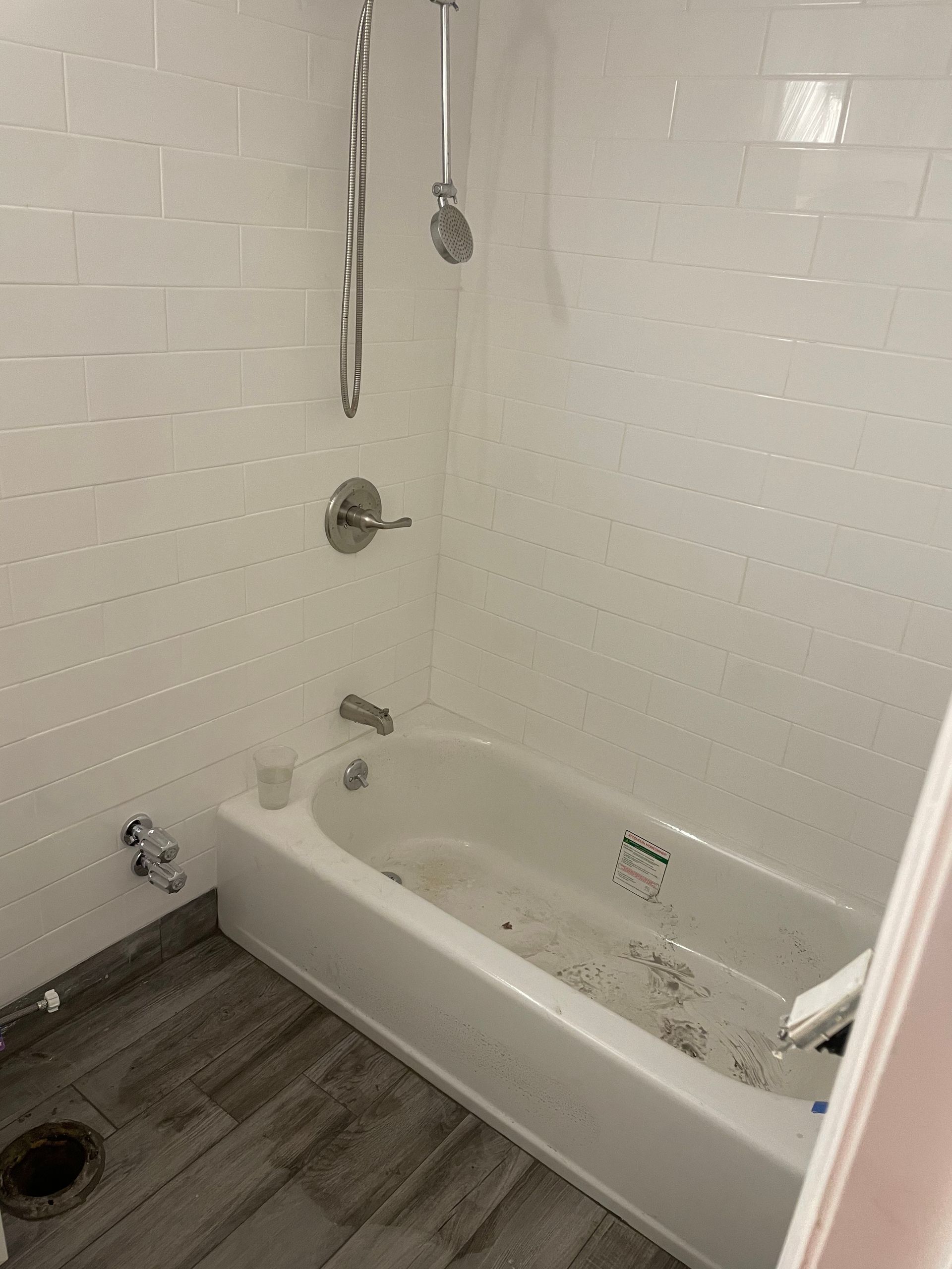 Small white bathroom with a tub-shower combo, gray floor, and visible staining in the tub and on the floor.