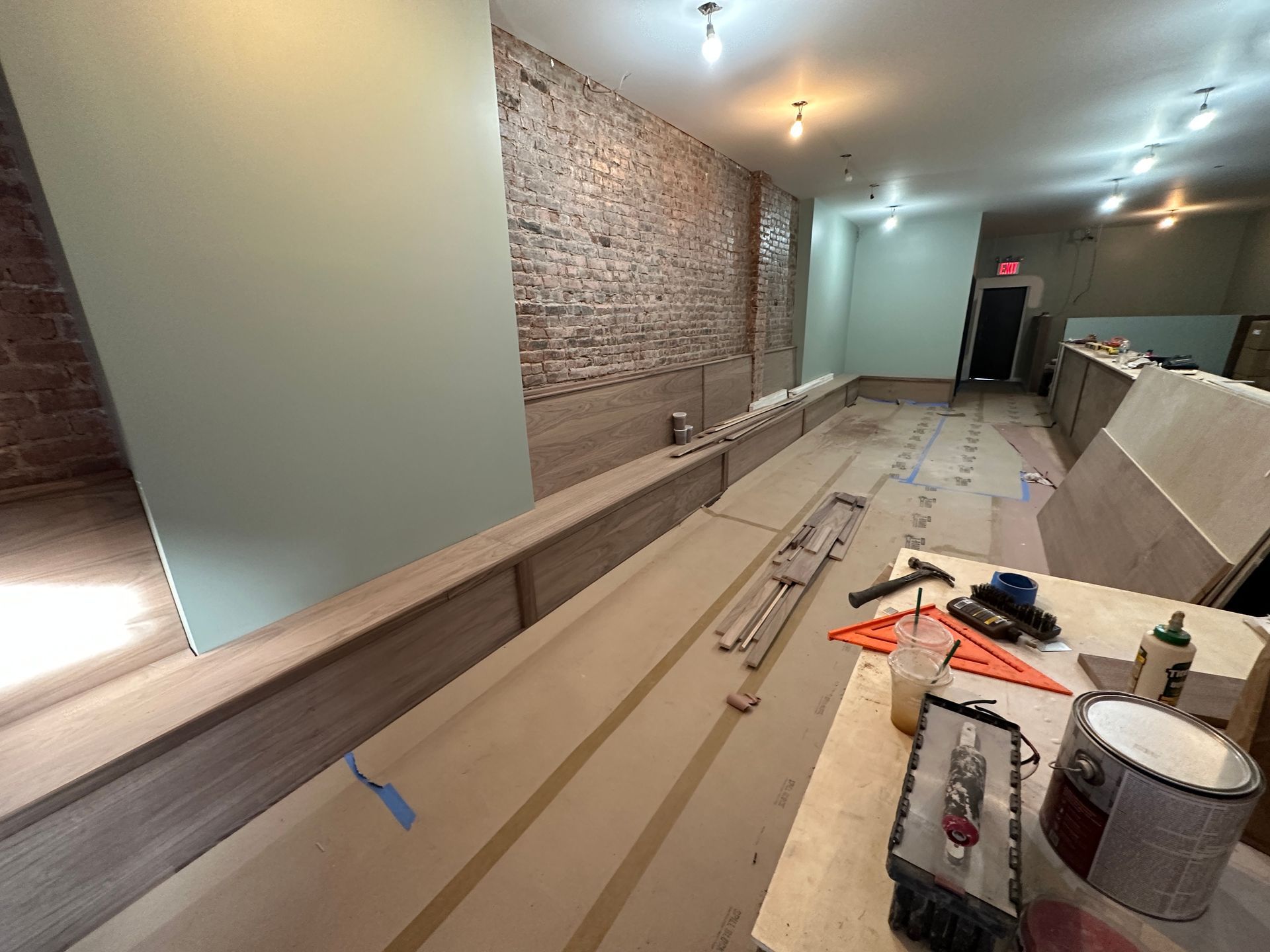 Long, narrow interior under renovation with exposed brick, built-in benching, and tools on the floor