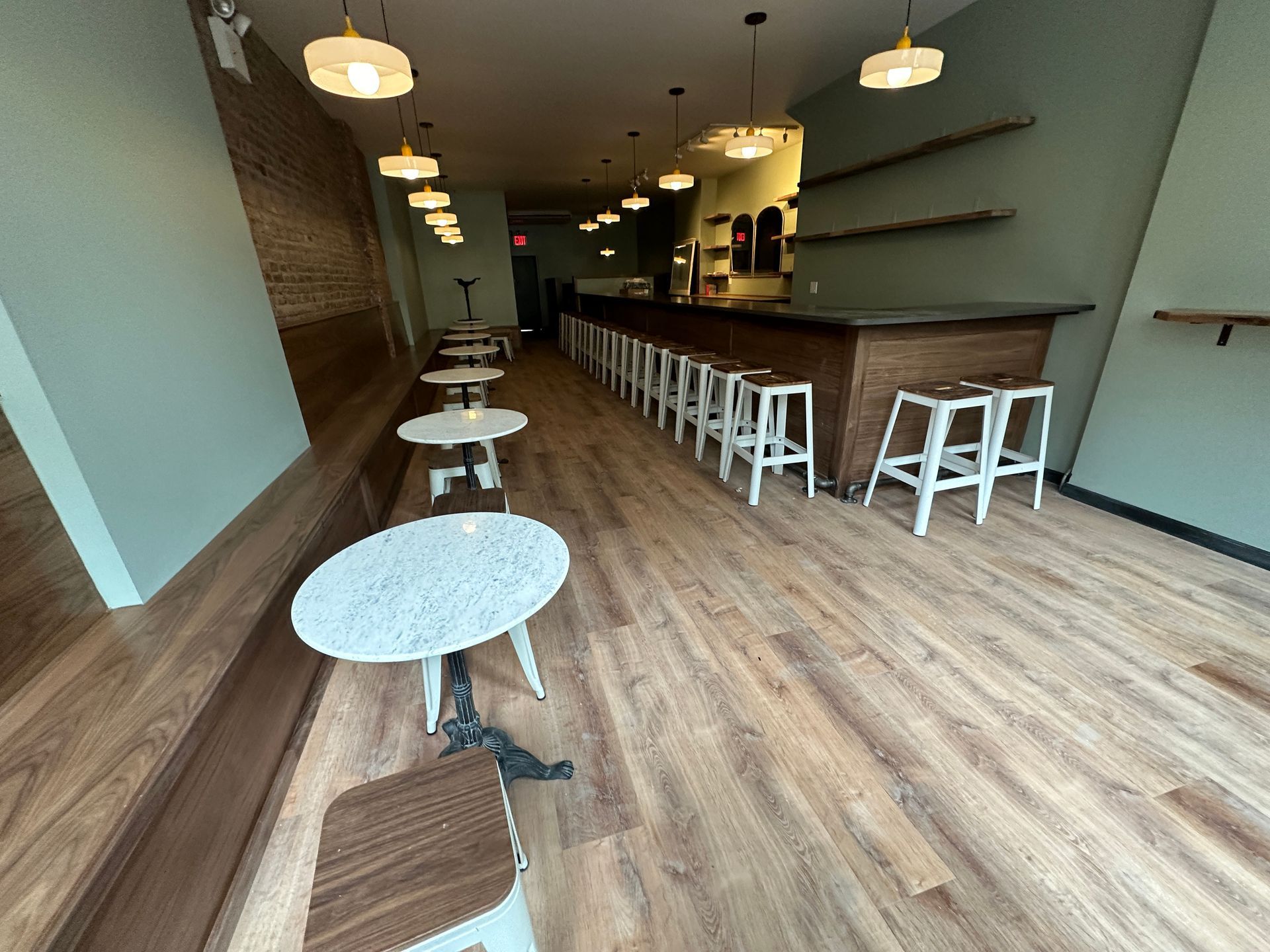 Empty modern café interior with wood floors, white stools, and pendant lights along the counter