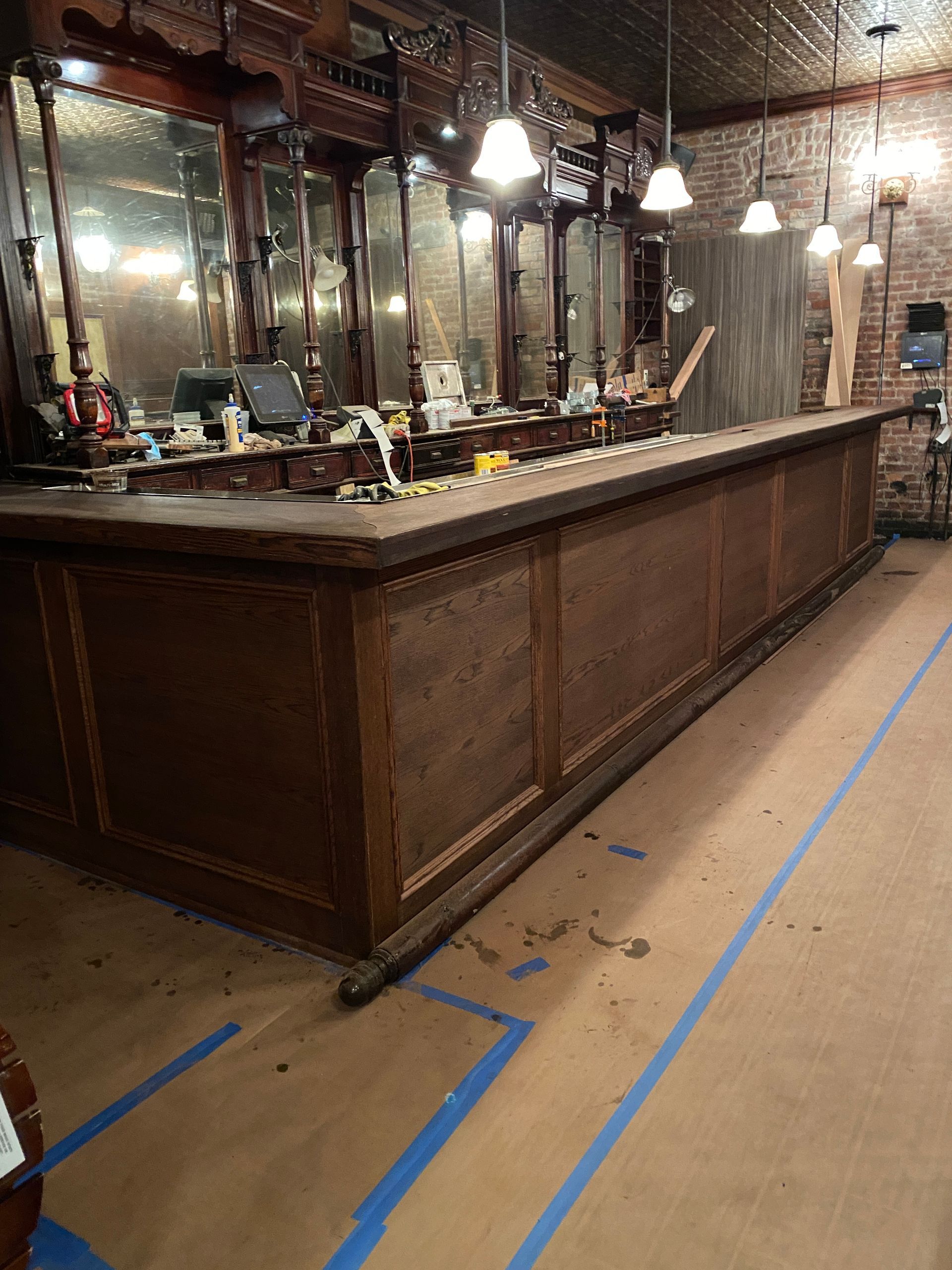 Empty bar interior with a long wooden counter, hanging lights, and blue floor markings