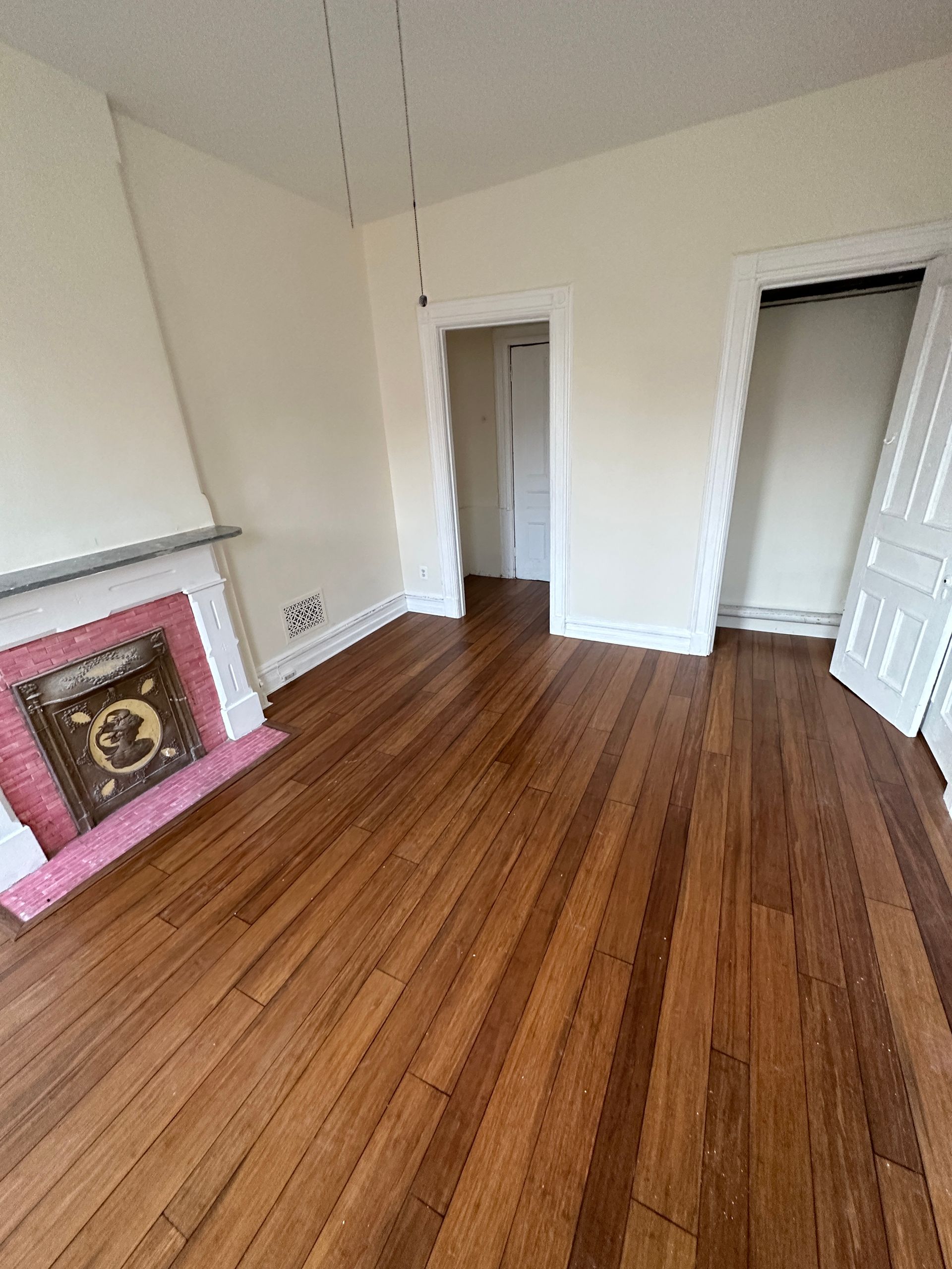 Empty room with hardwood floors, white walls, and a pink fireplace surround