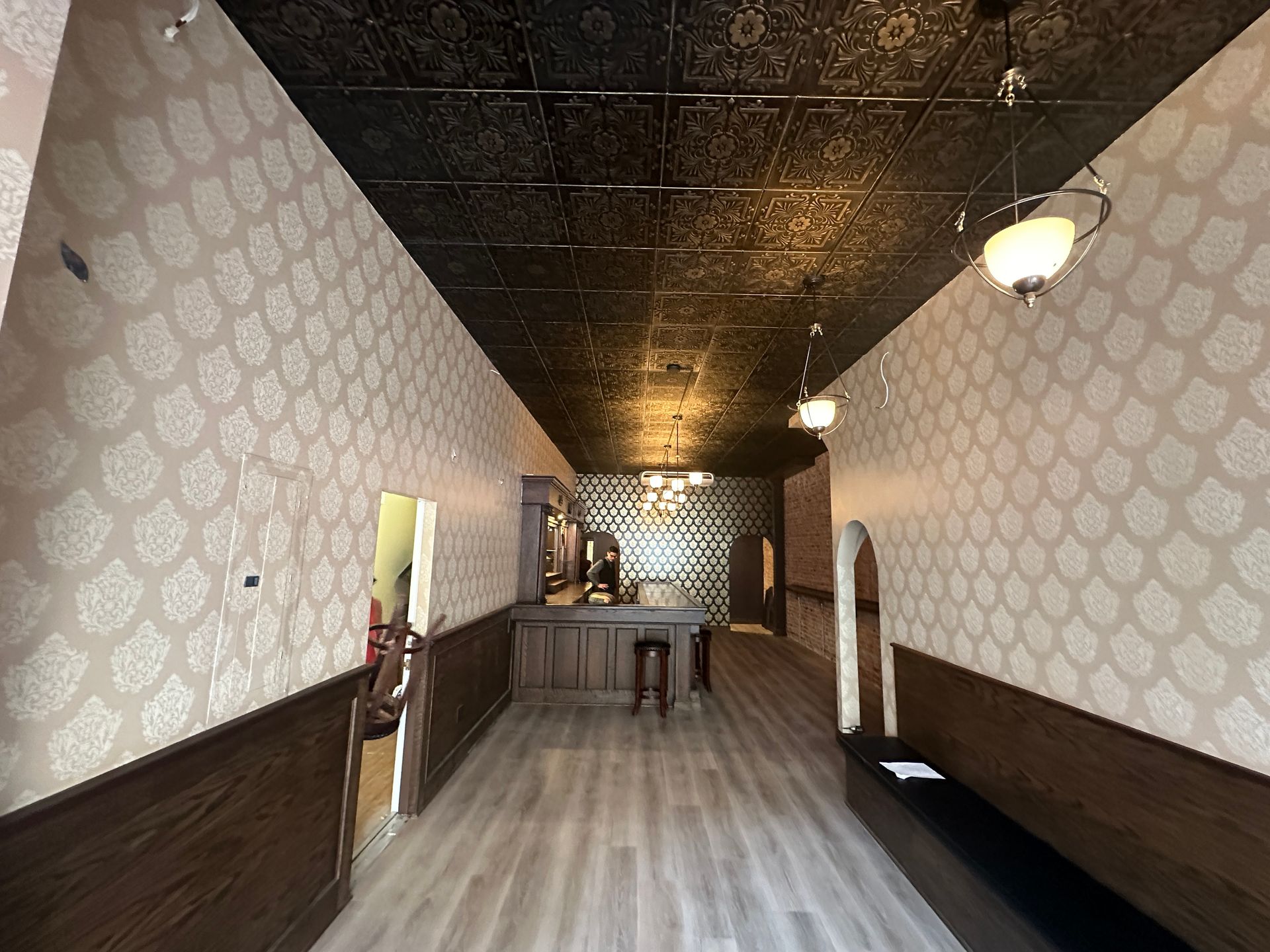 Empty vintage hallway with patterned wallpaper, dark wood trim, and hanging lights