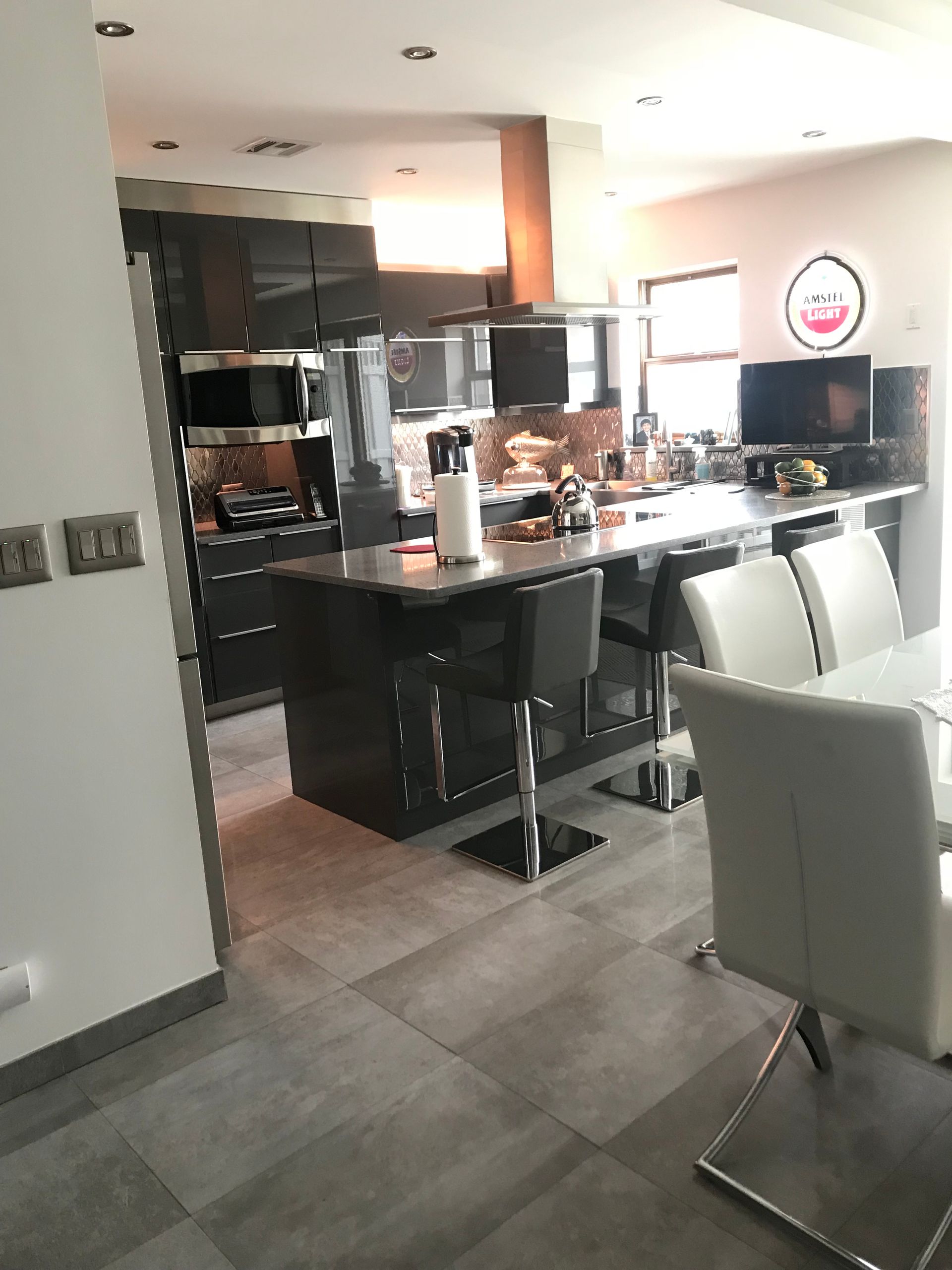 Modern kitchen and dining area with a central island, black bar stools, and white chairs near a window.