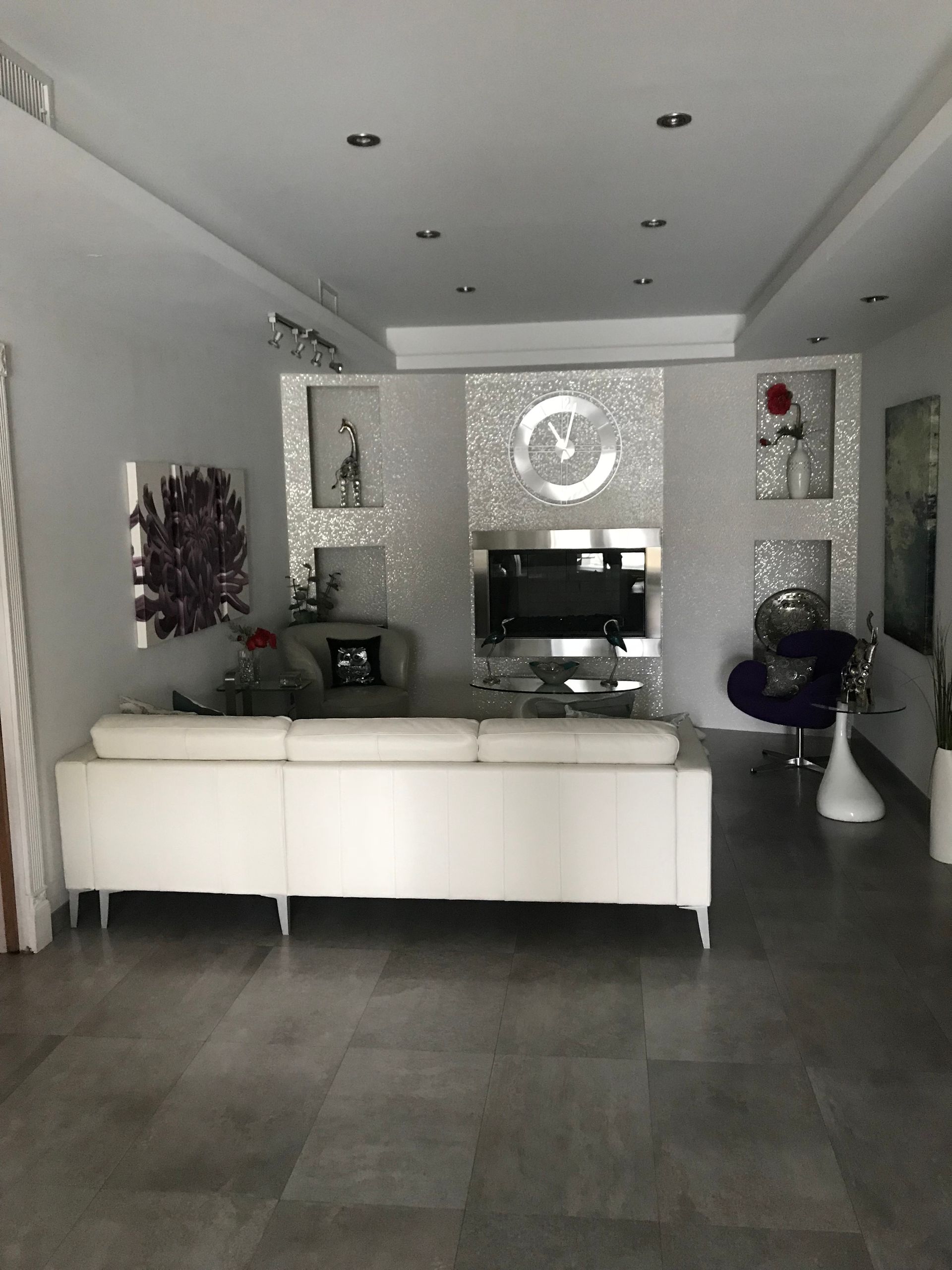 Modern living room with white sofa, dark tiled floor, wall-mounted TV, and decorative shelving