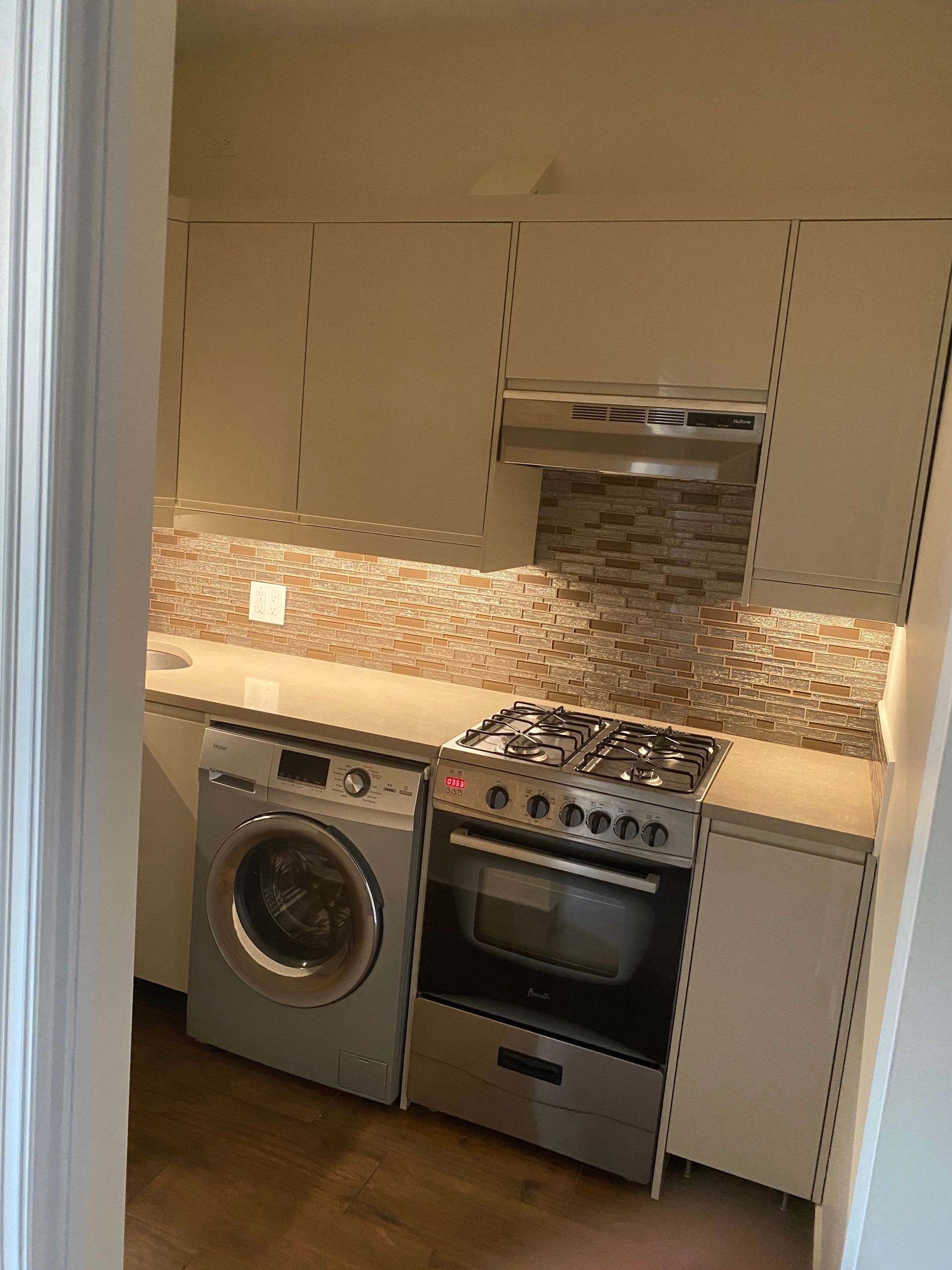 Small kitchen with beige cabinets, tiled backsplash, countertop, washing machine, and stainless steel oven.