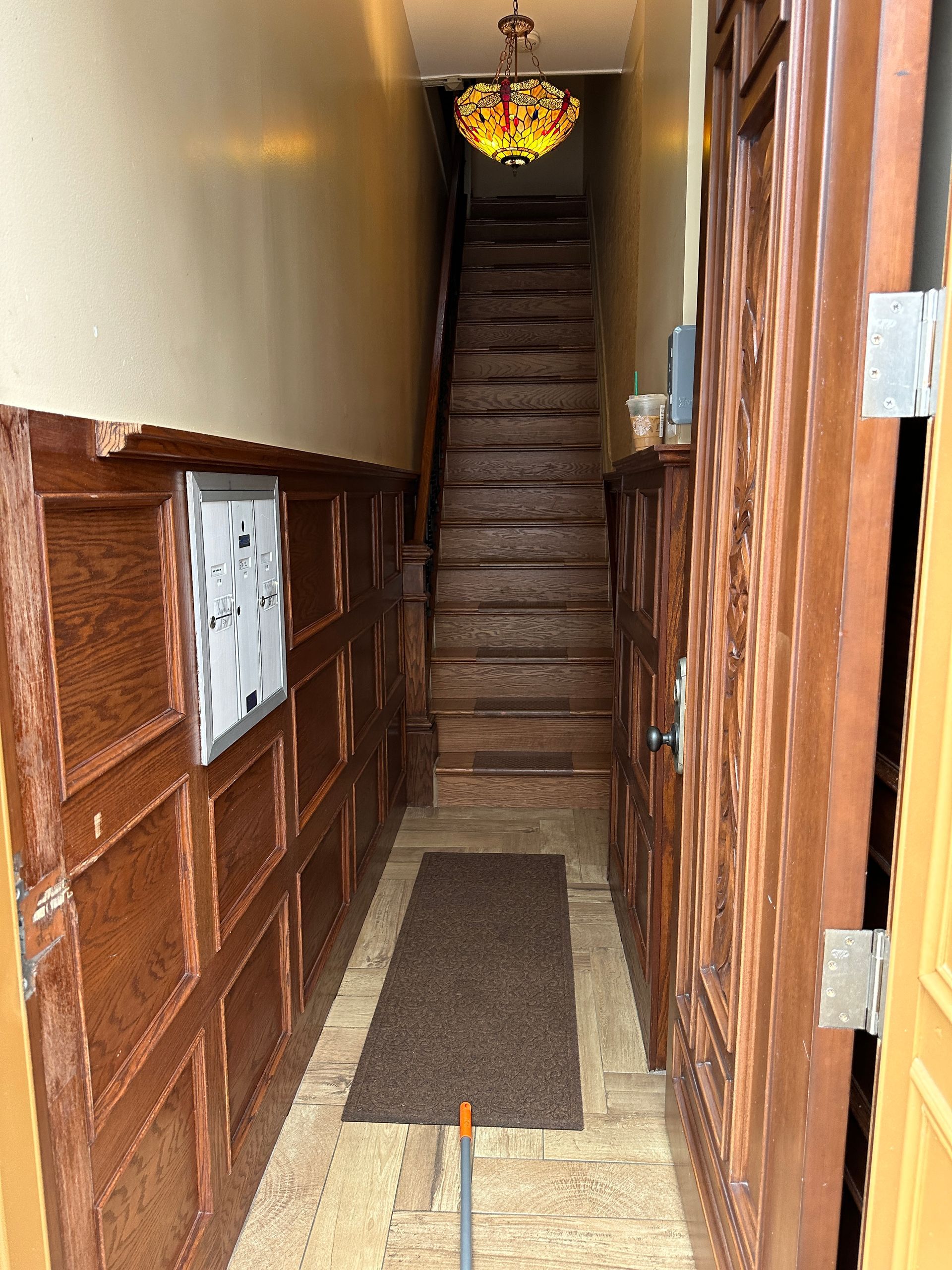 Narrow hallway with wood paneling, a staircase at the end, and a small rug on the floor.