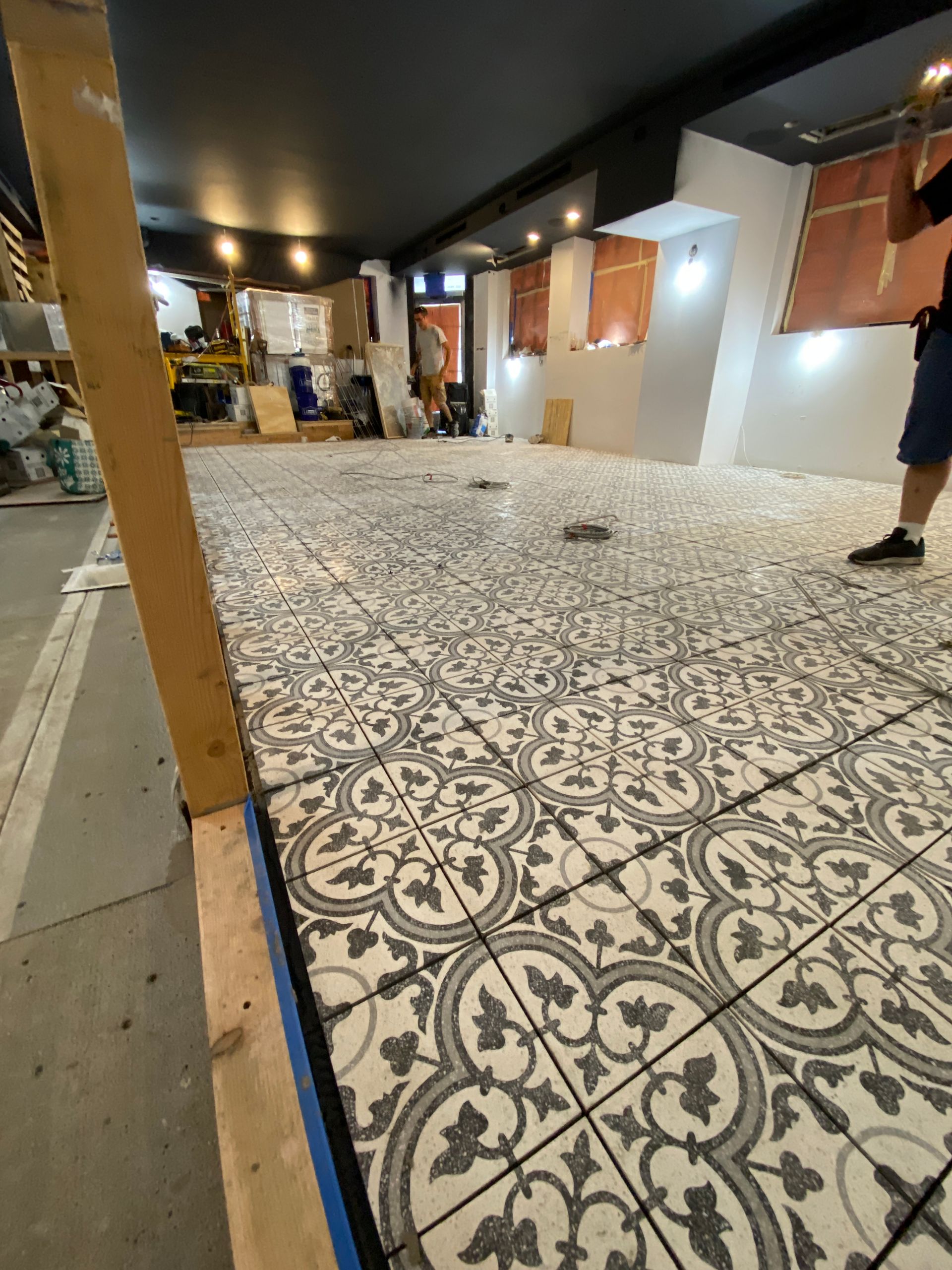 Patterned tile floor in a dim indoor hallway with people and construction materials in the background