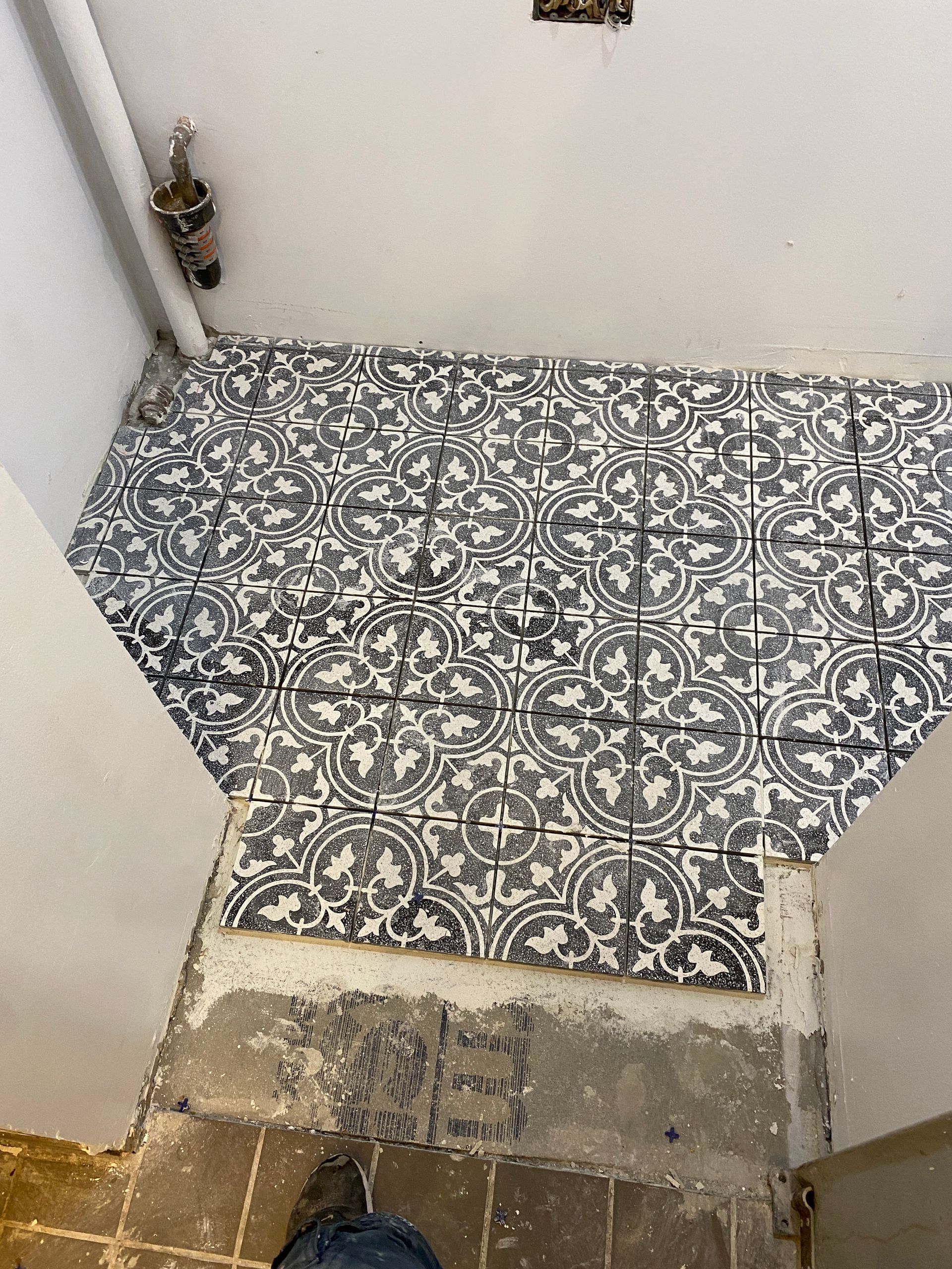 Small tiled shower floor with black-and-white patterned tiles and a dirty, worn threshold.
