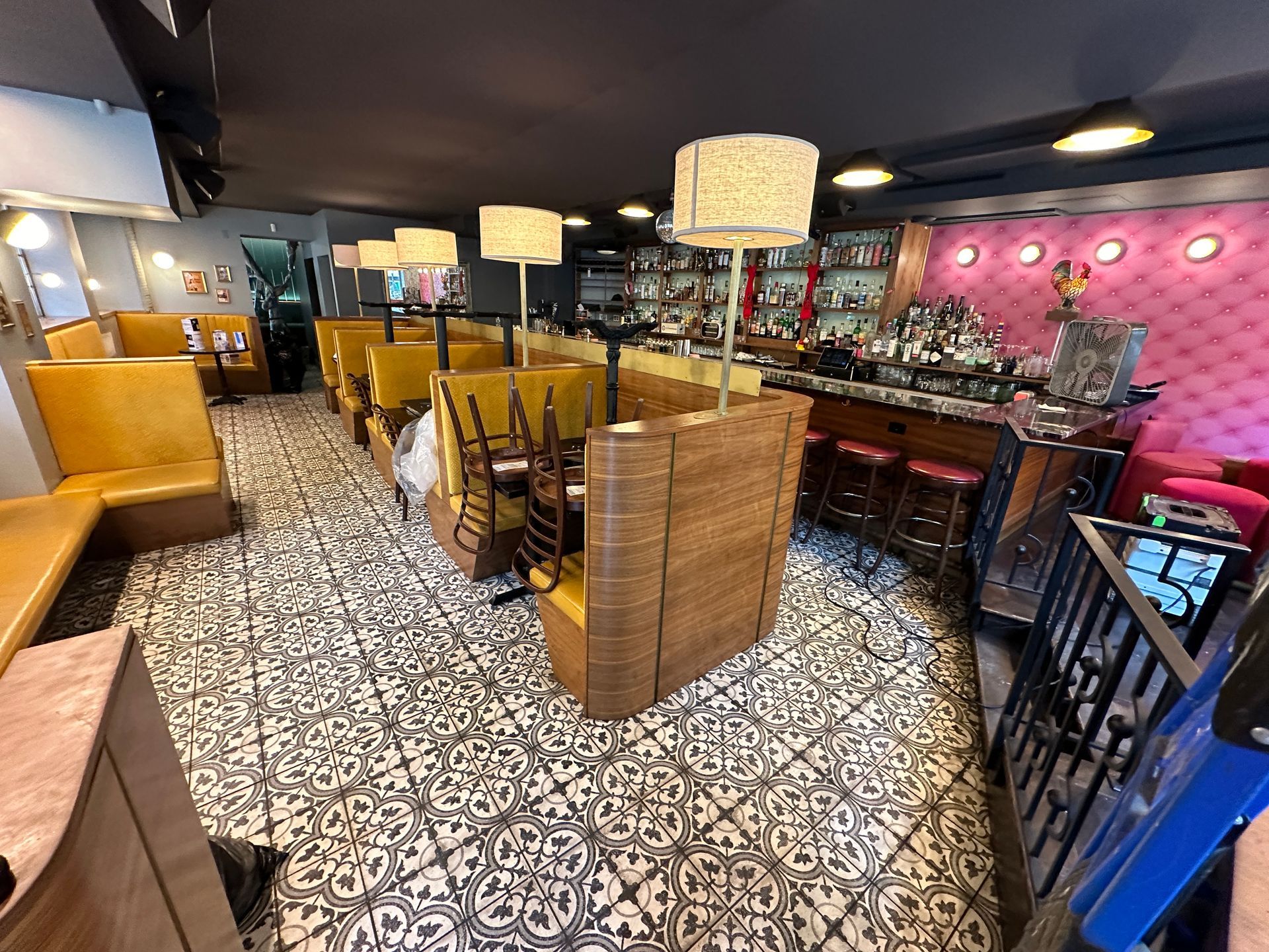 Cozy lounge with patterned floor, yellow chairs, bar stools, and pink wall décor