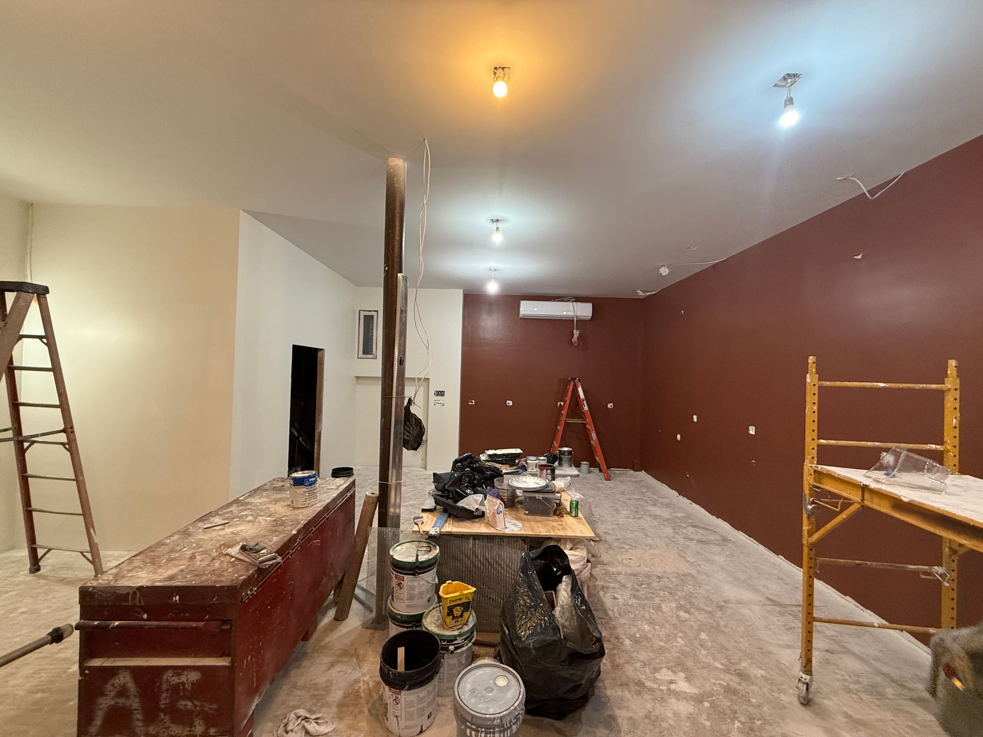 Partially renovated room with ladder, scaffold, tools, and maroon accent wall