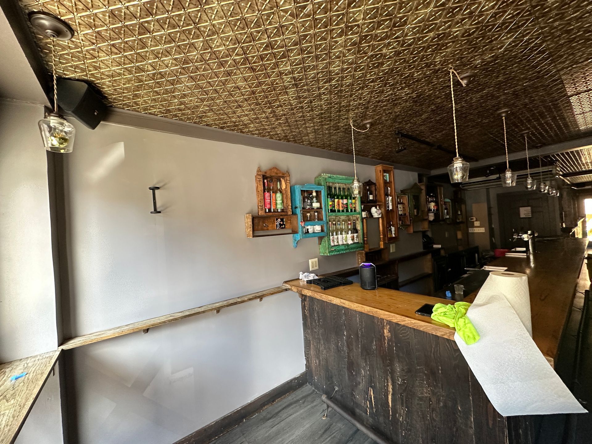 Empty rustic bar interior with dark counter, wall shelves, and textured ceiling