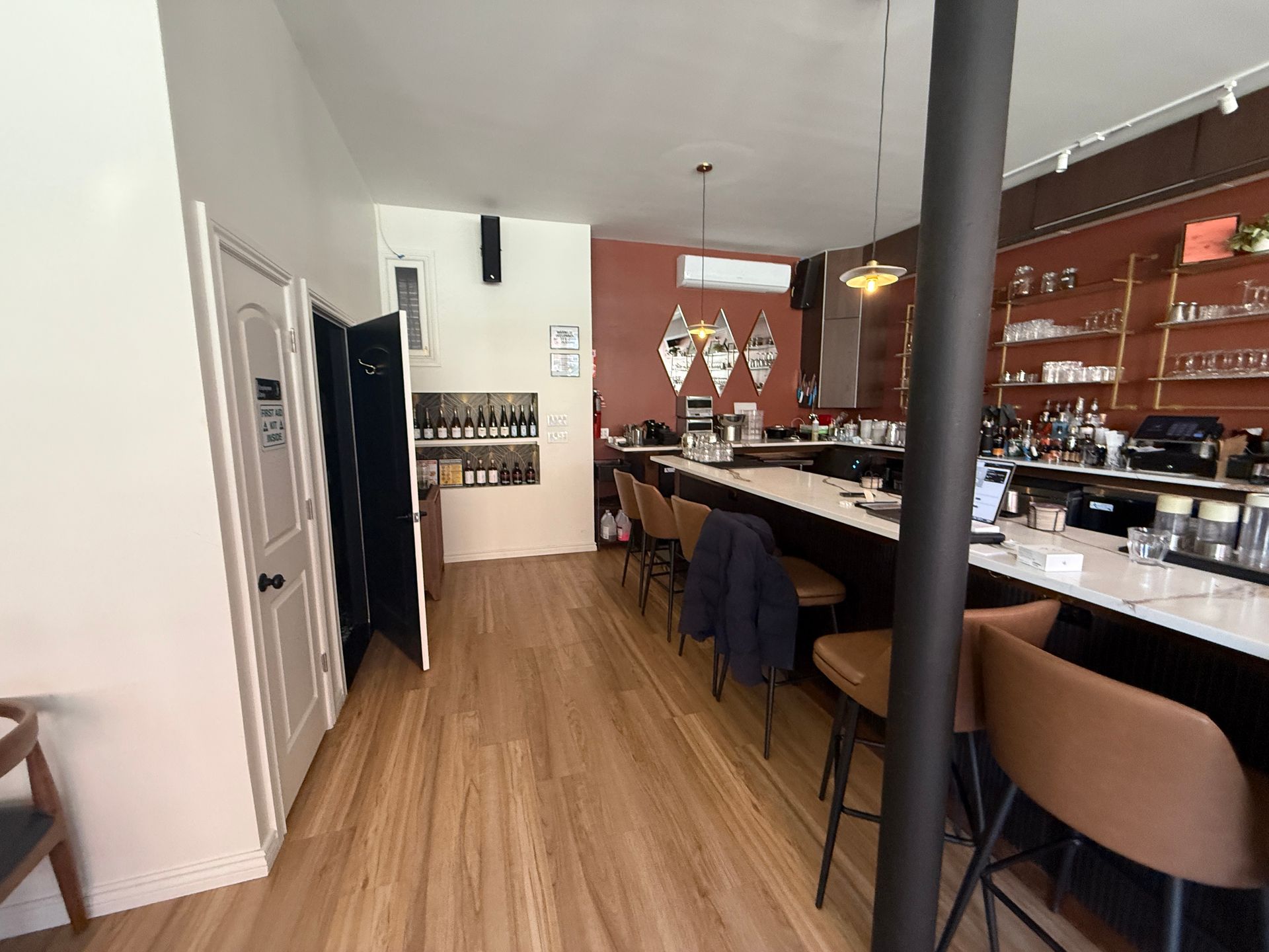 Modern café interior with wood floors, bar counter, stools, and shelves behind the counter