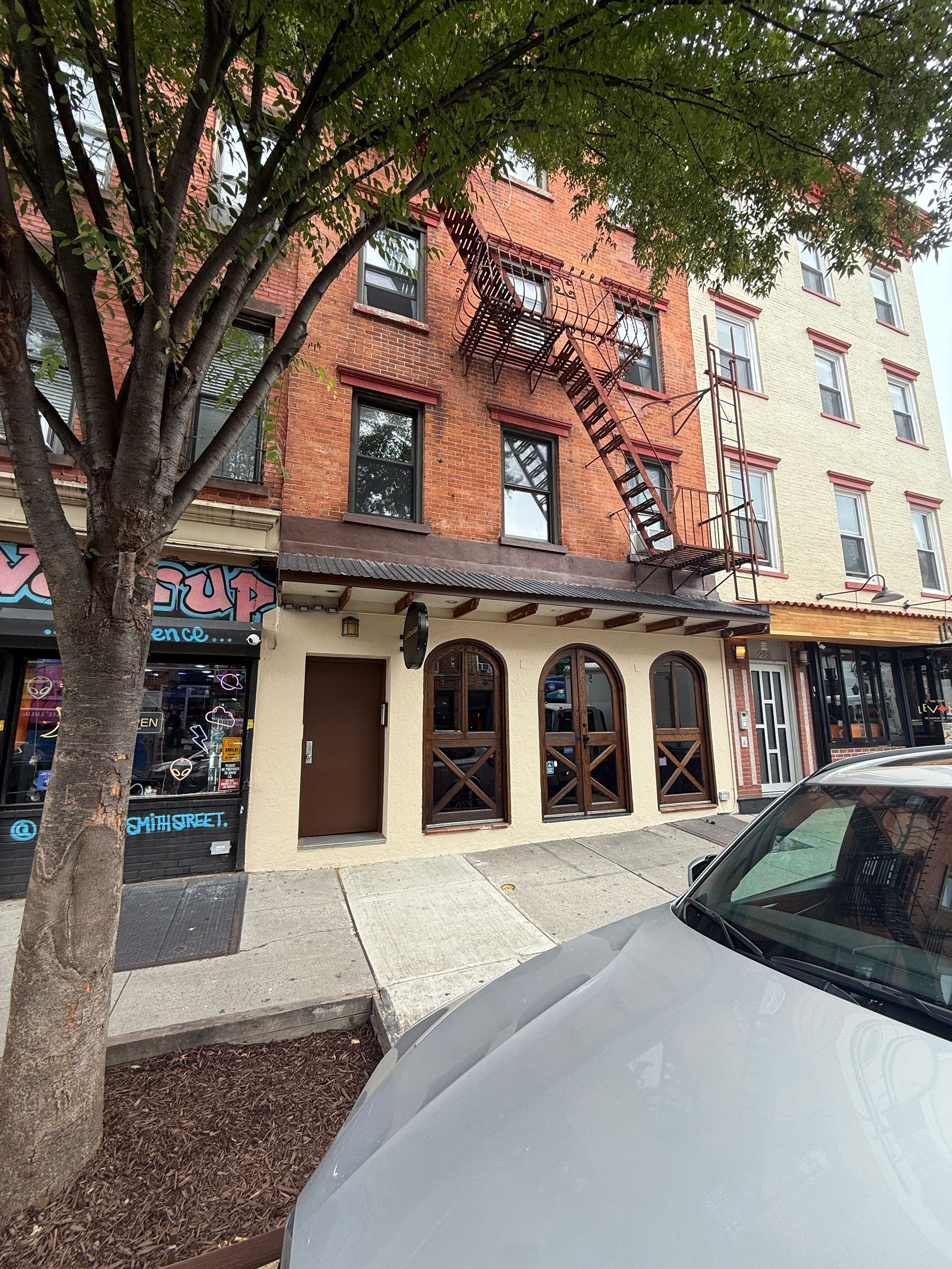 Brick apartment building with arched storefront windows, tree-lined sidewalk, and parked cars in front
