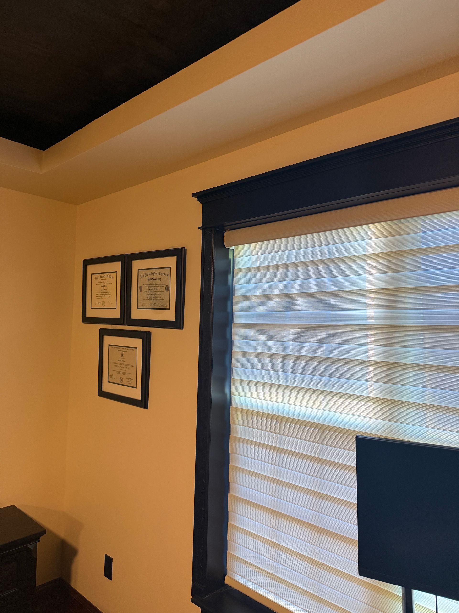 Wall with framed certificates beside a window with blinds and a small TV in a softly lit room