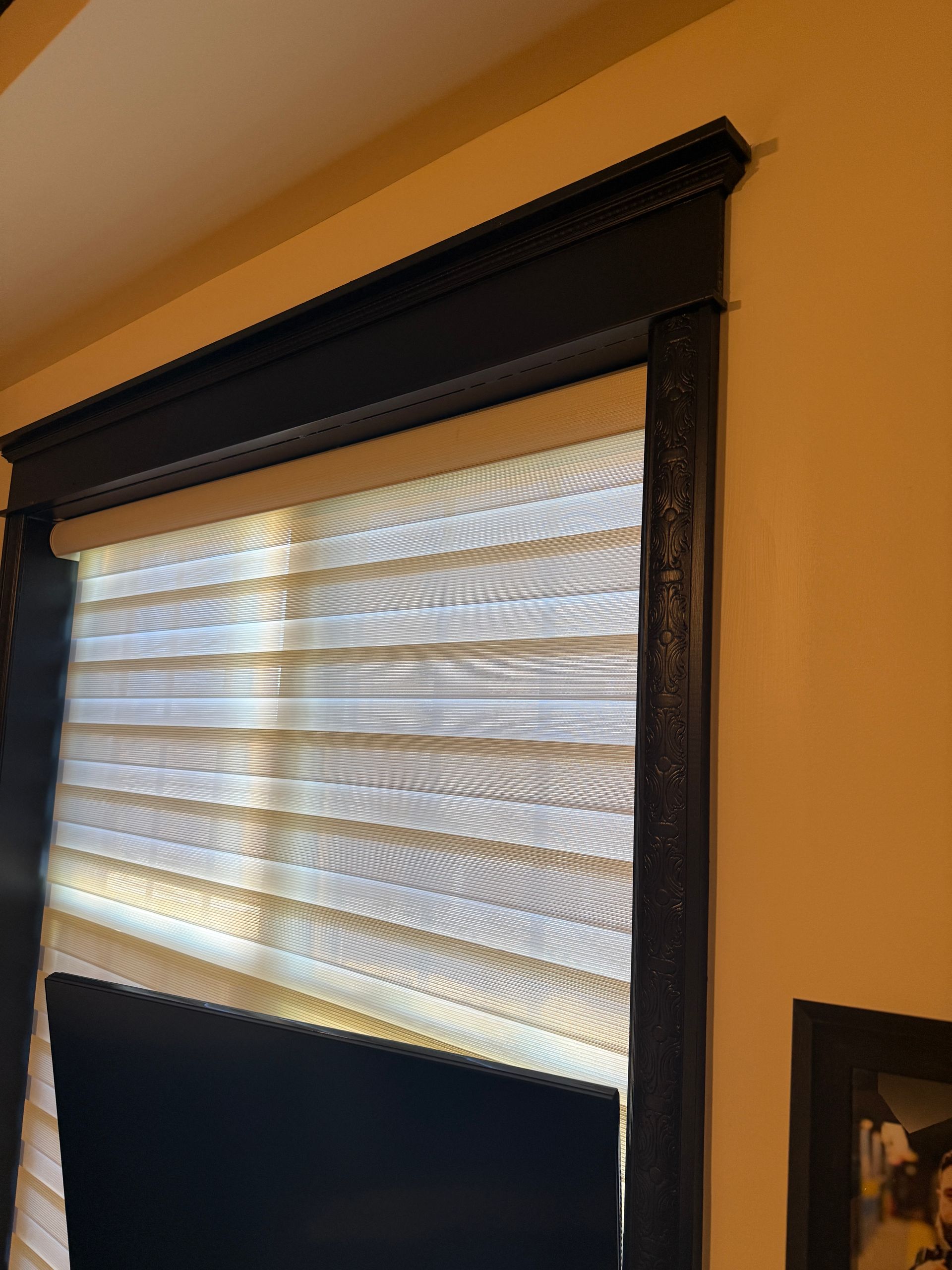 Close-up of a black window blind with white pleated shade on a tan wall