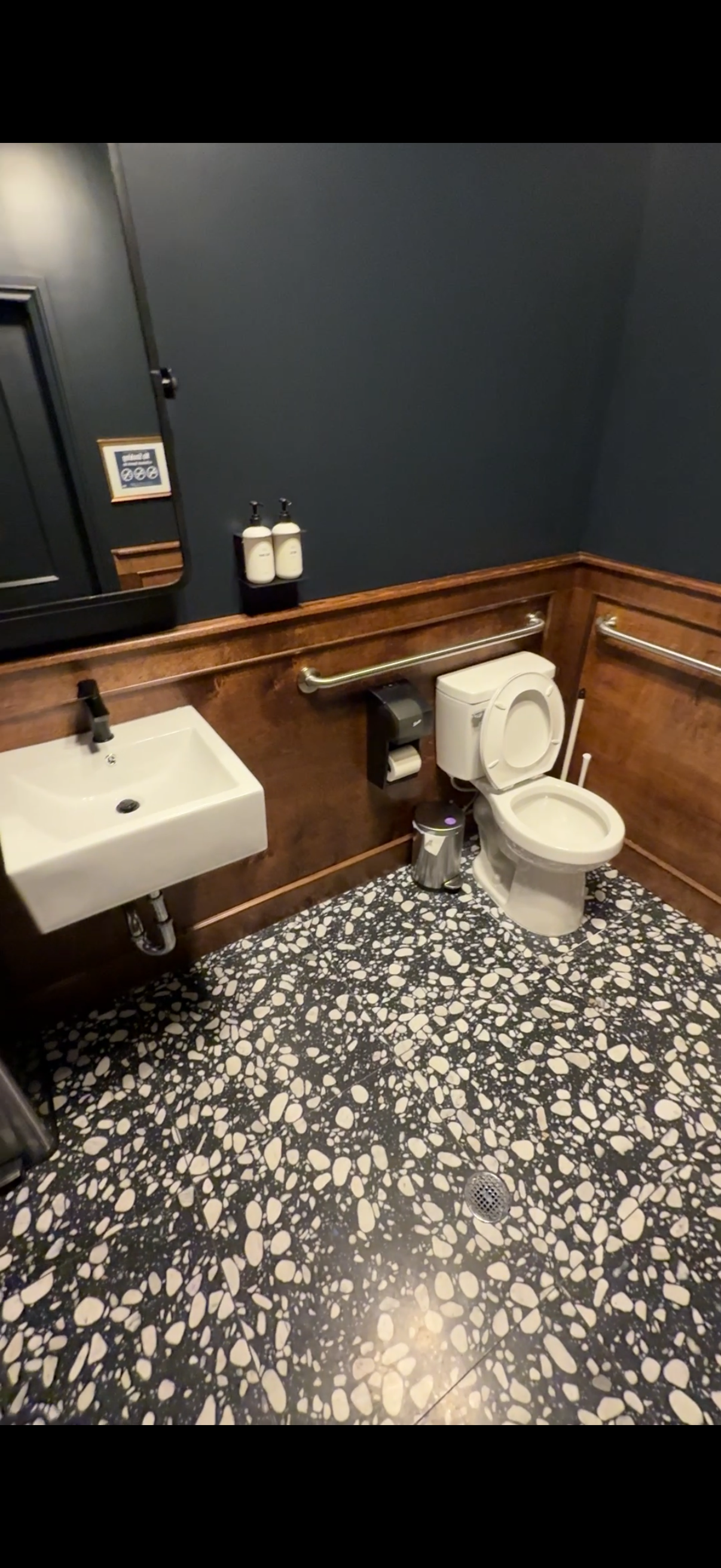 Small restroom with toilet, white sink, dark blue walls, wood trim, and black-and-white patterned floor.