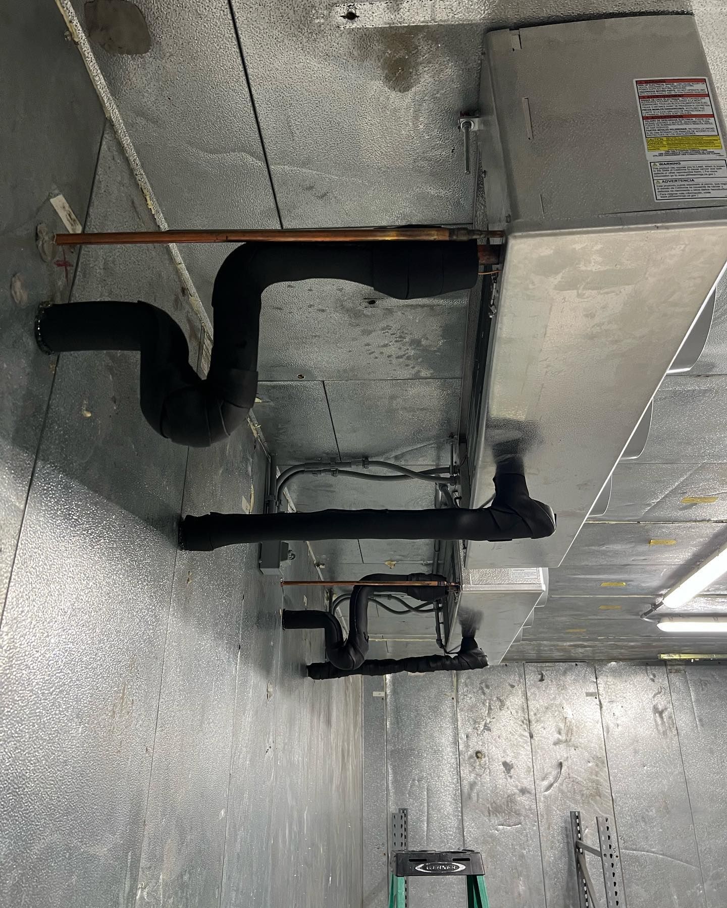 A room with a ladder and pipes hanging from the ceiling.