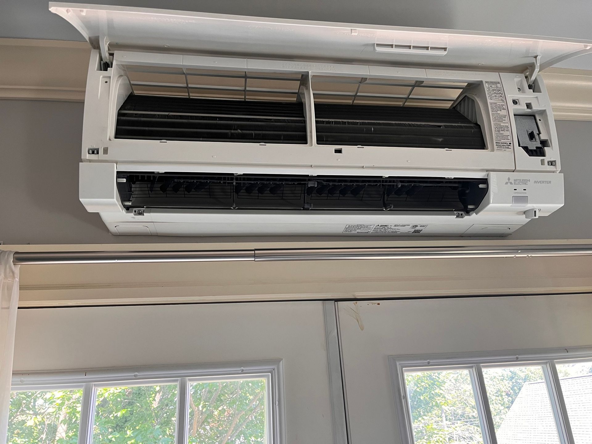 A white air conditioner is hanging from the ceiling in a room next to a window.