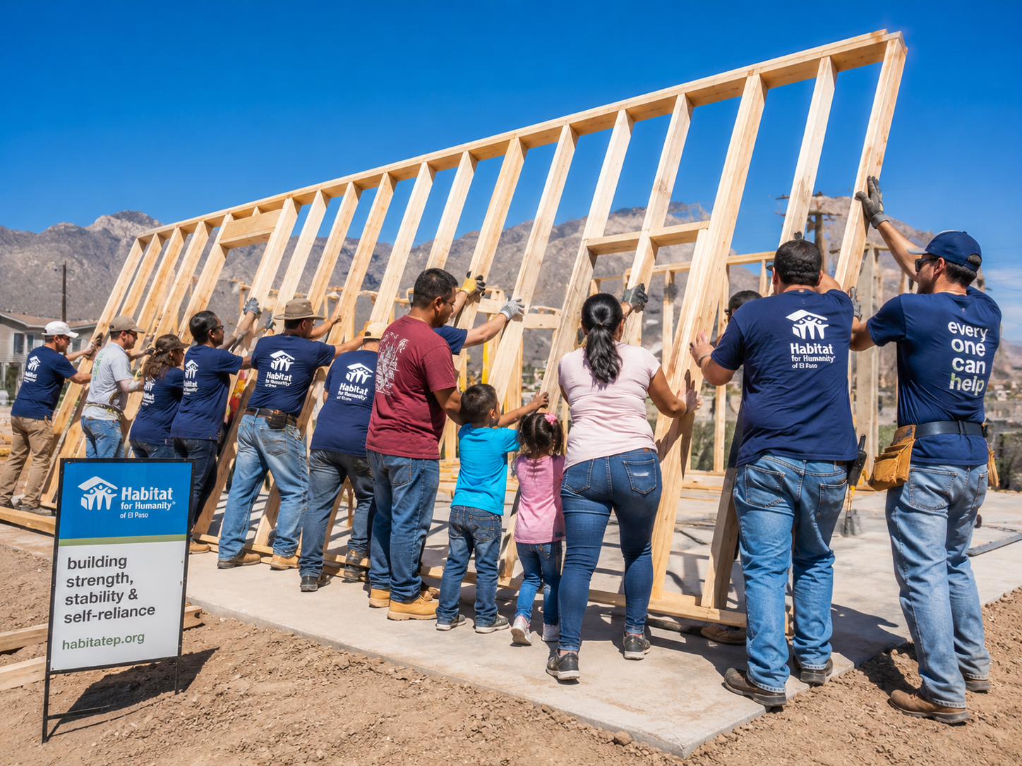 Volunteers and a family raise a new home wall frame beneath a bright El Paso sky.