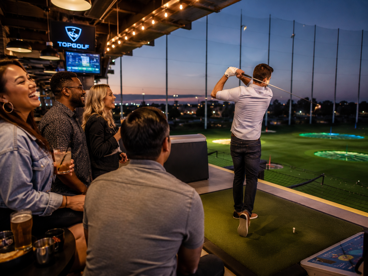 Friends laugh as one golfer takes a swing at a Topgolf bay during a fun evening event.