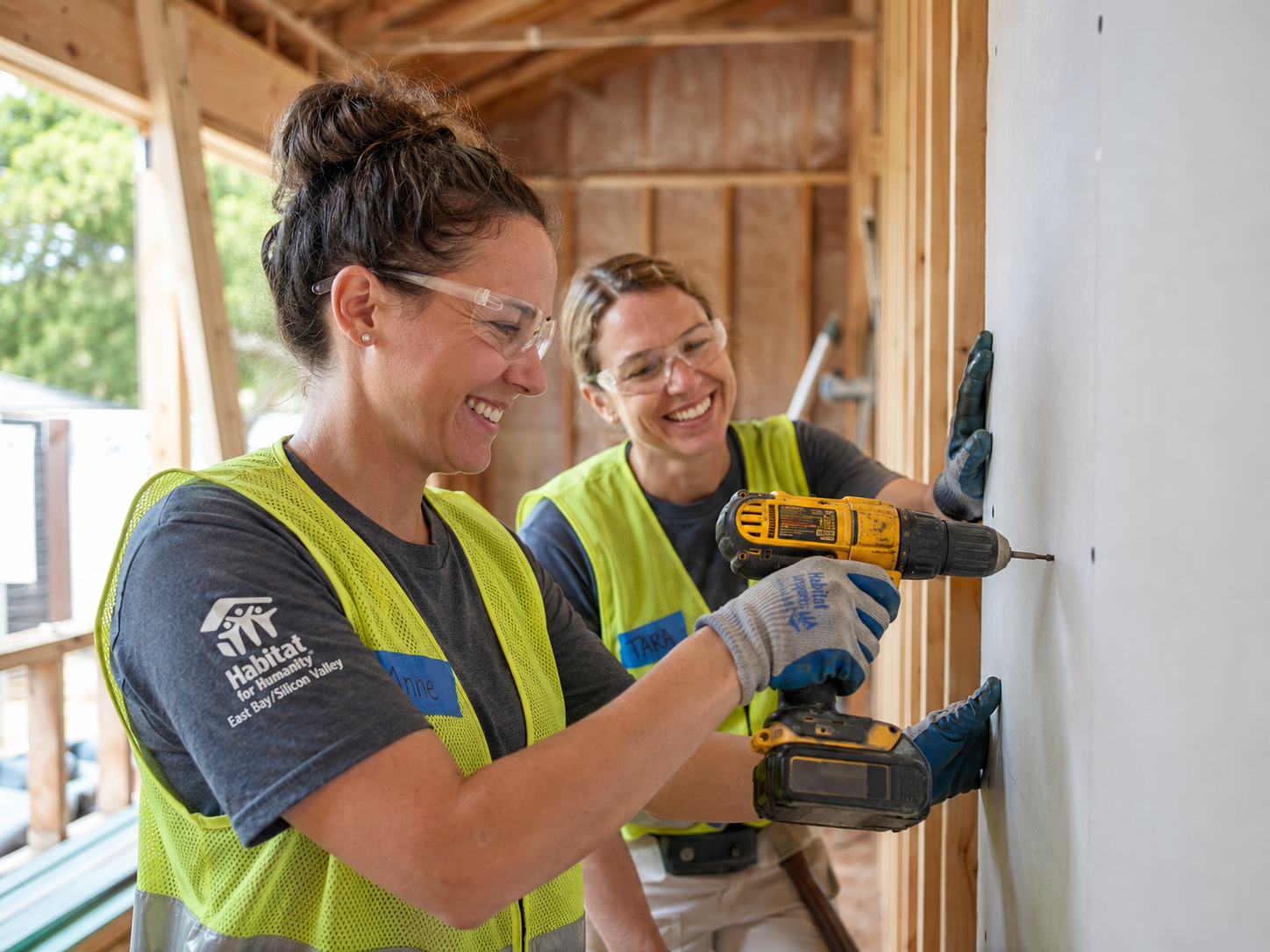 Volunteers install drywall in a Habitat for Humanity home using a cordless drill.