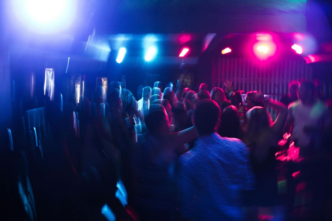 A crowded dance floor filled with people under vibrant blue and pink stage lights.