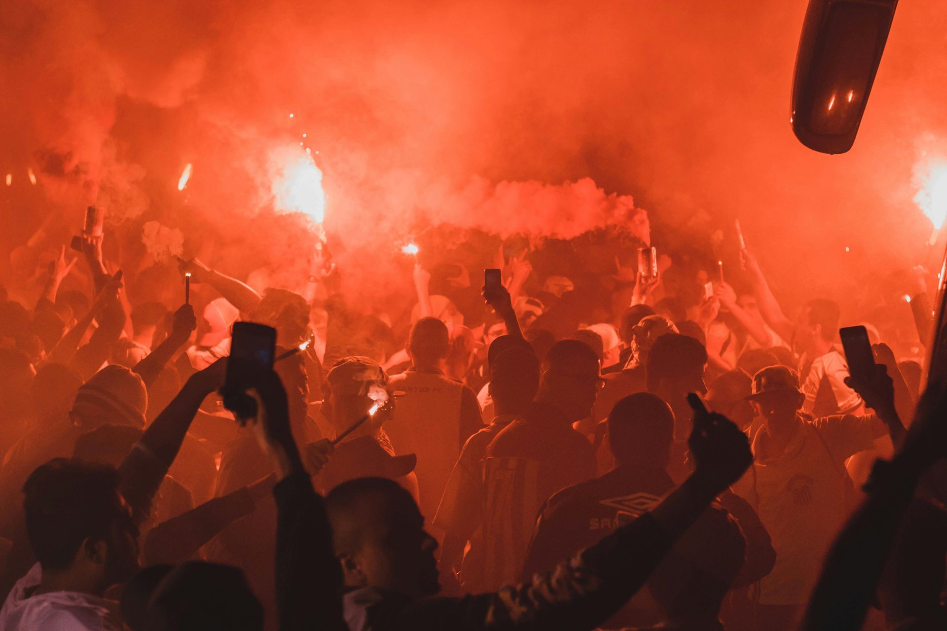 A dense crowd of people holding lit flares and phones, creating a hazy, intense red atmosphere in a dimly lit setting.