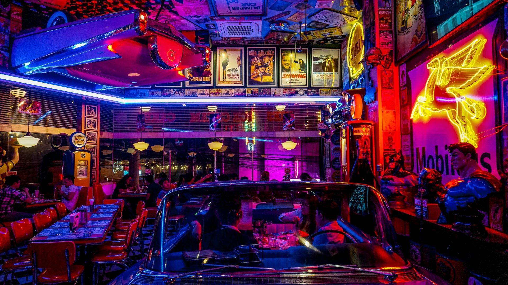 A vibrant, neon-lit retro diner featuring classic car booths, vintage movie posters, and nostalgic décor.