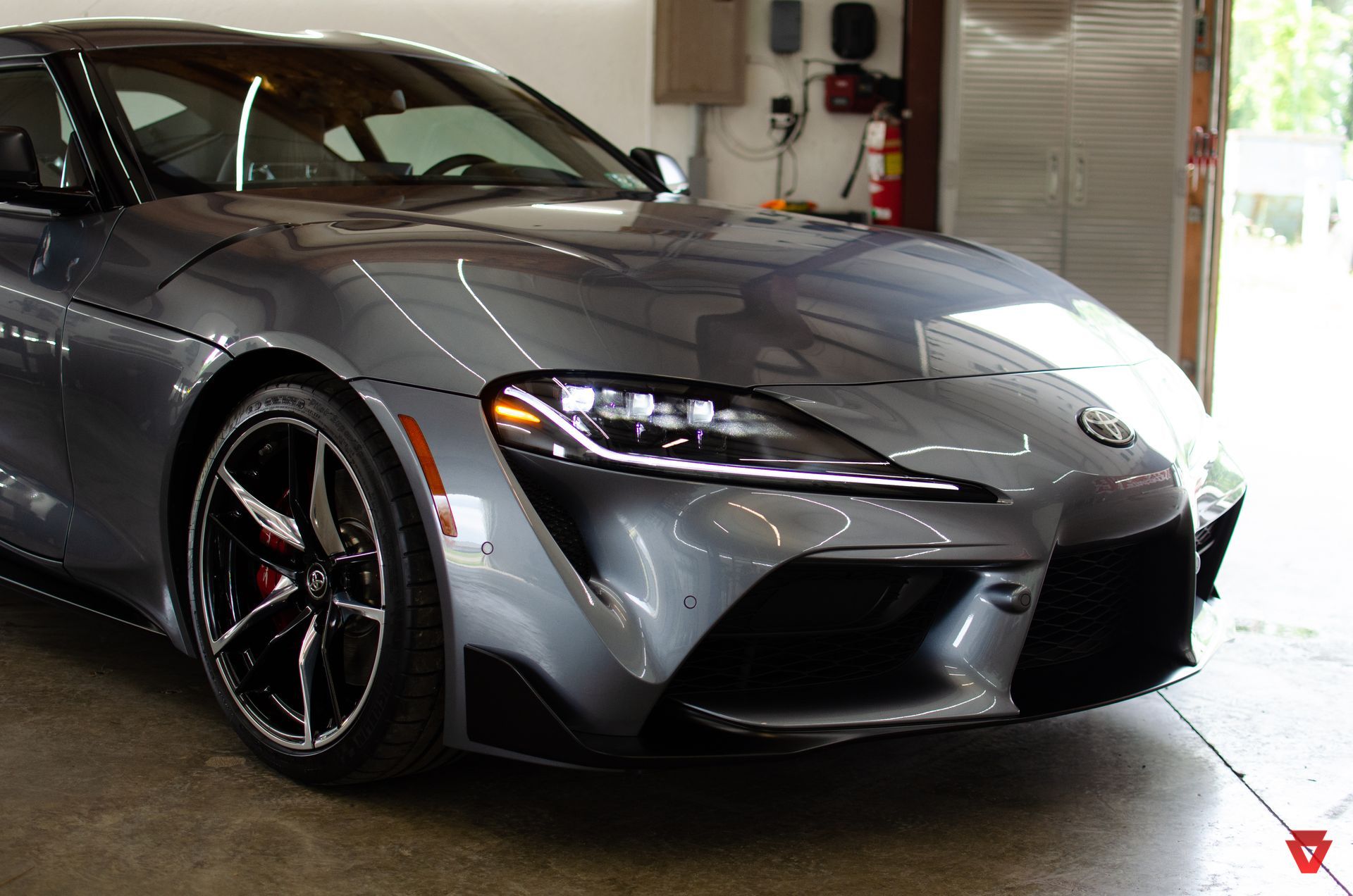 Silver sports car parked in a garage, front-left view with headlights on