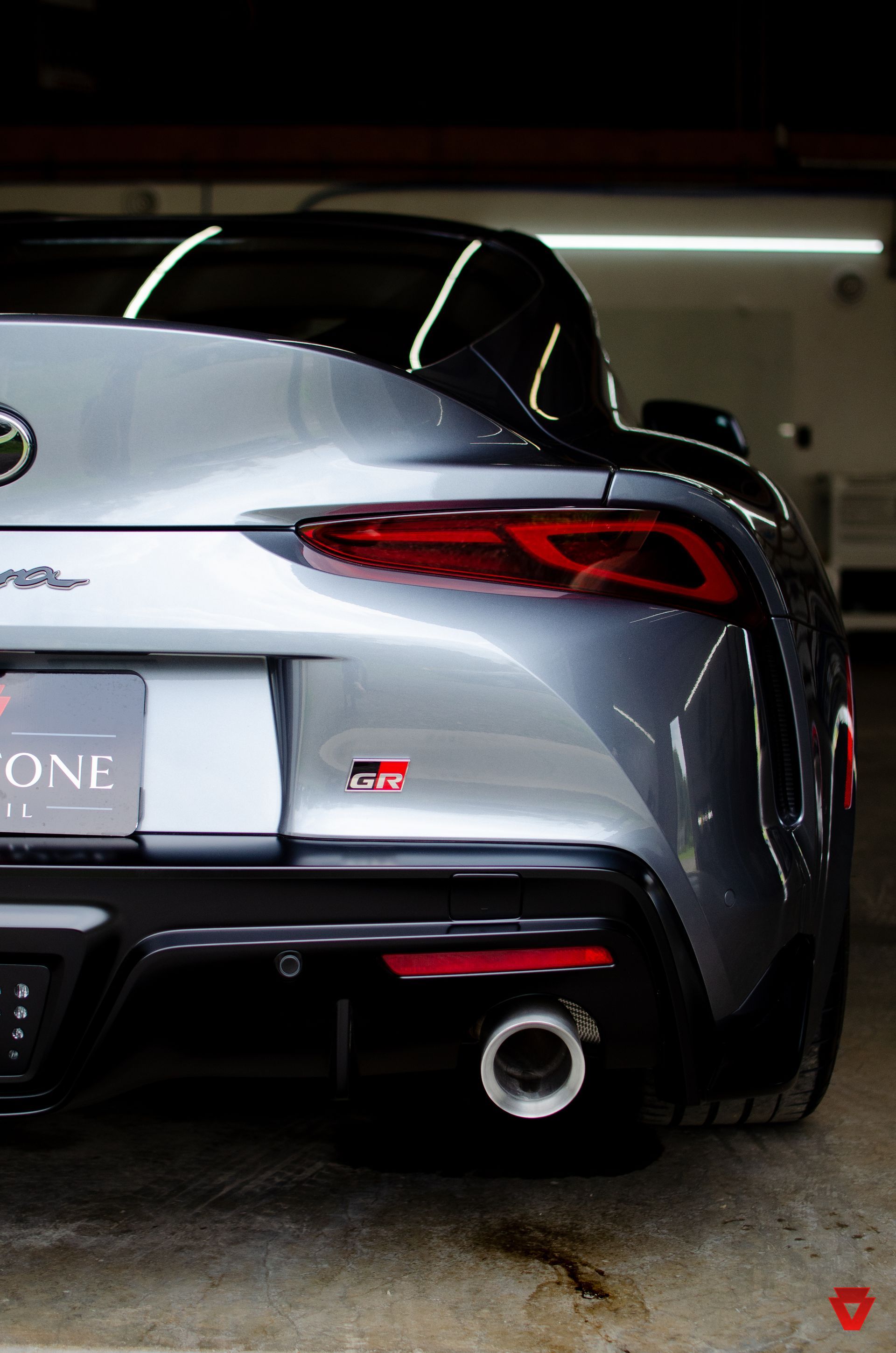 Rear view of a silver sports car with red taillights parked in a garage.
