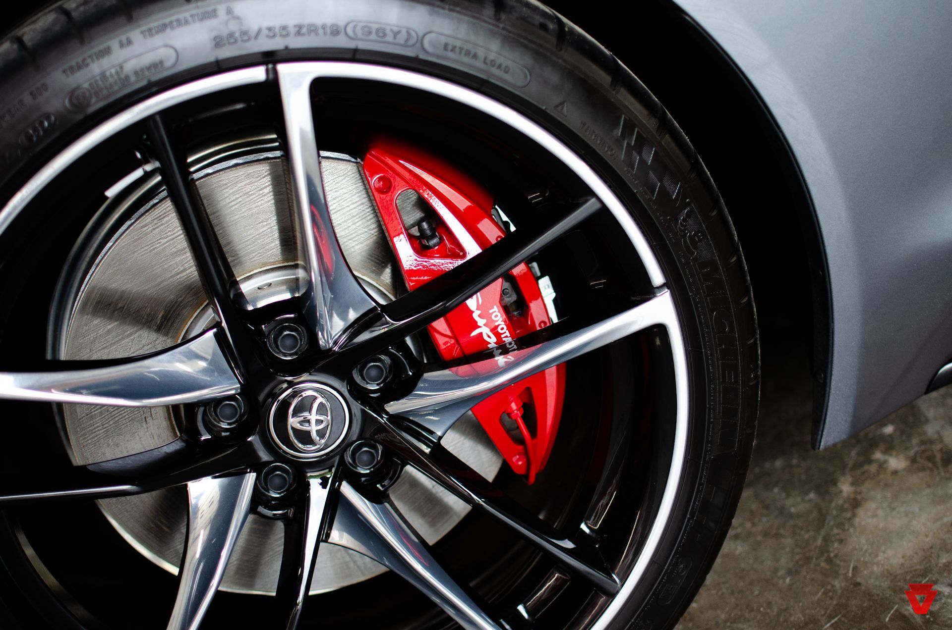 Close-up of a car wheel with black alloy rim and red brake caliper behind it
