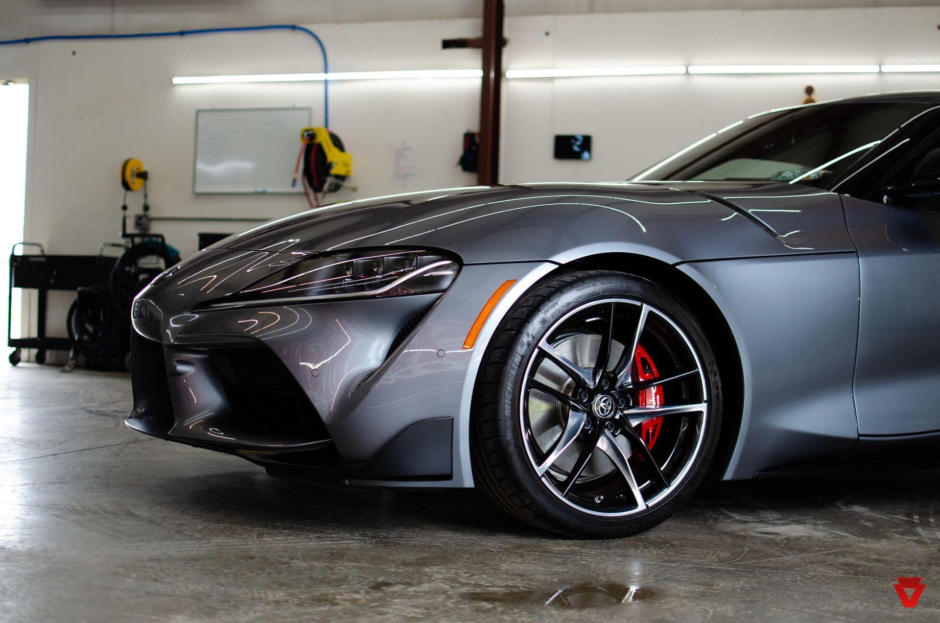 Gray sports car in a garage, front view with red brake calipers and polished wheels