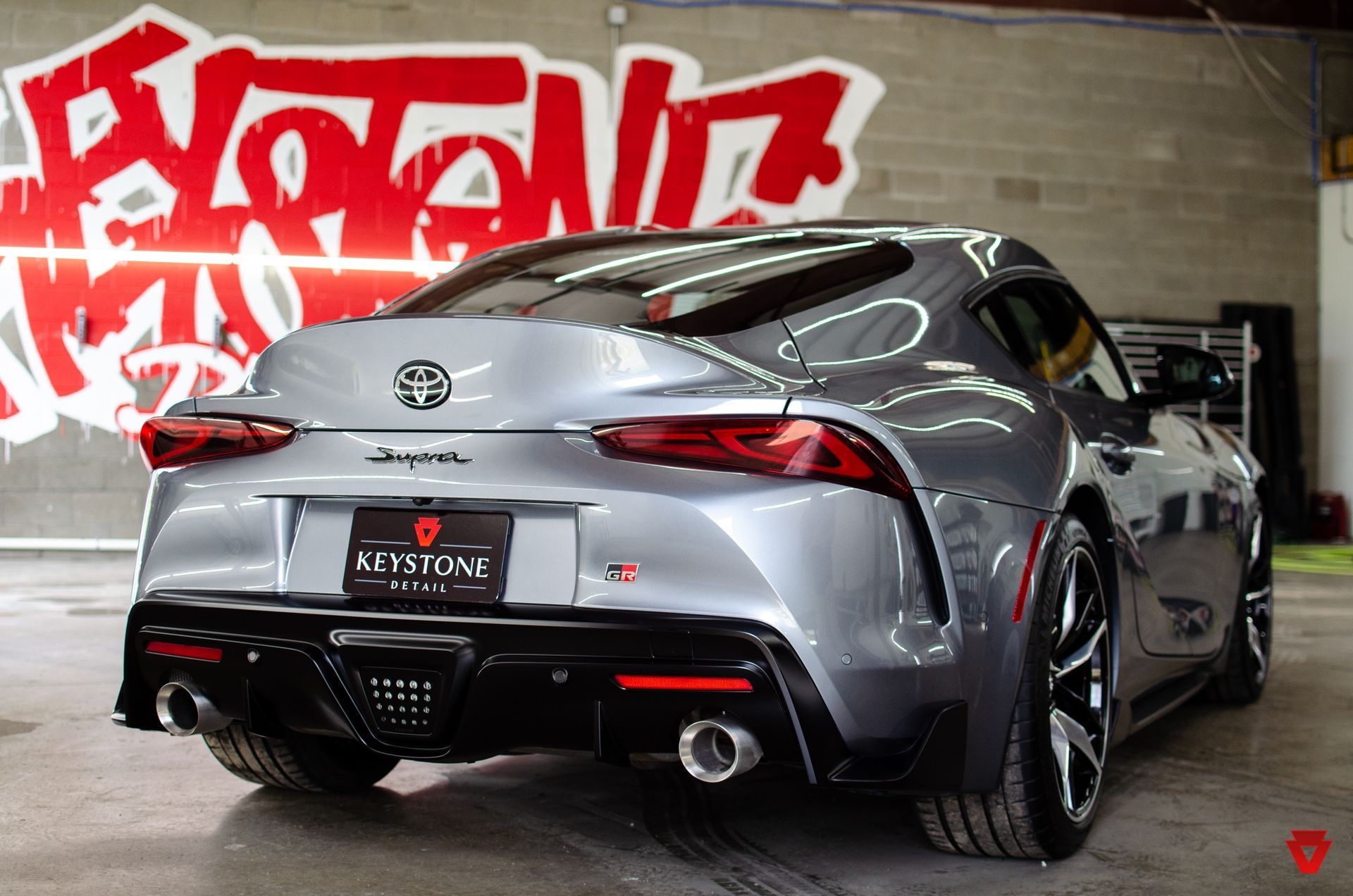 Silver sports car parked indoors against a graffiti wall, rear view