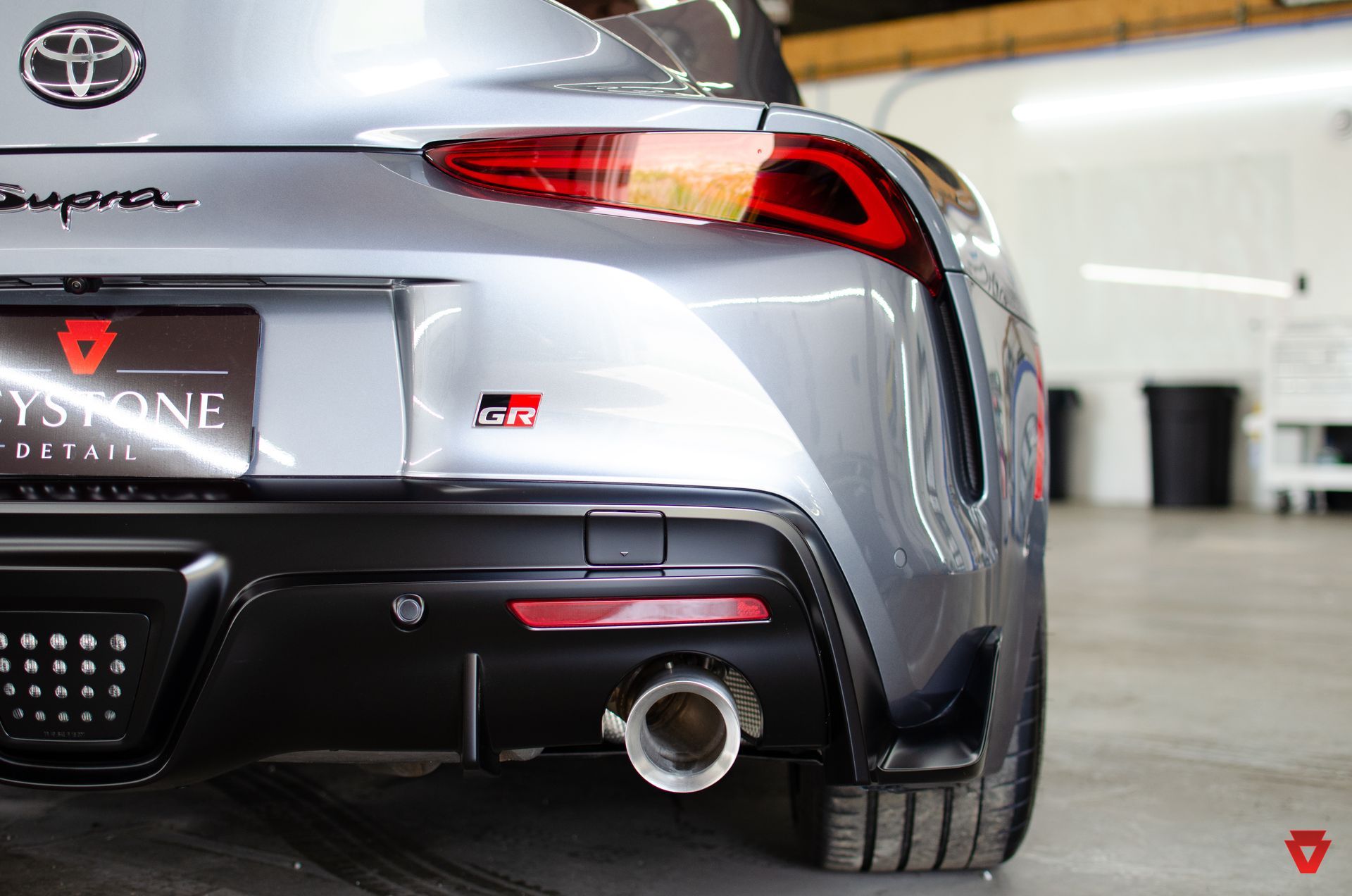 Rear view of a silver Toyota Supra with red taillights and a single exhaust in a garage