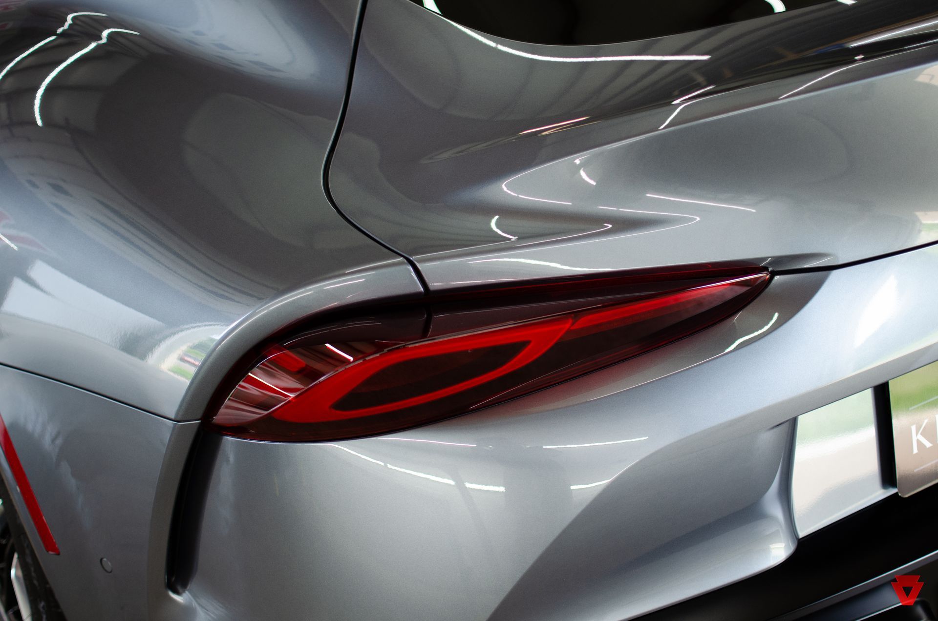 Close-up of a silver sports car’s rear, showing a sleek red taillight and curved bodywork